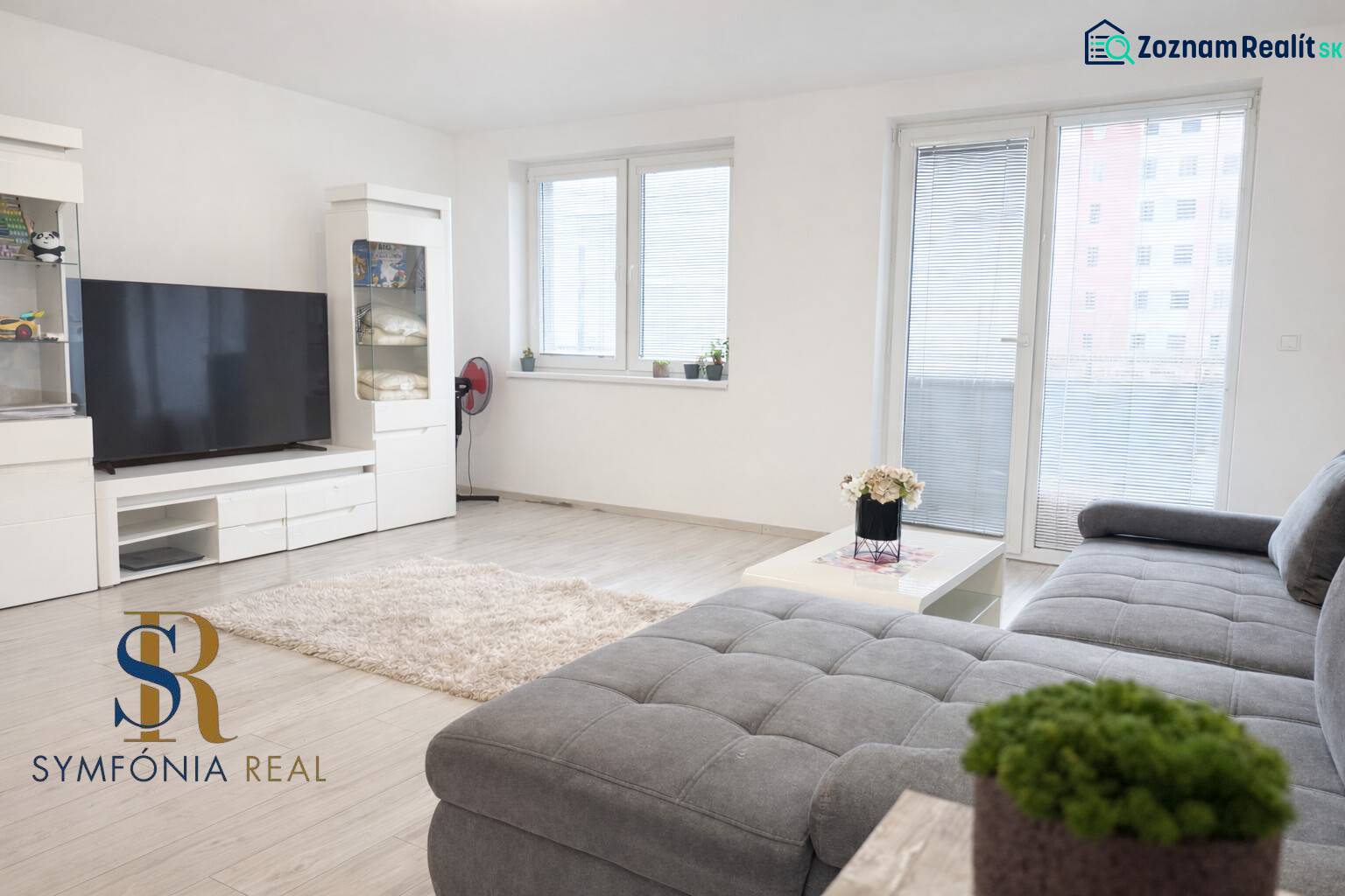 2-izbový byt novostavba s podzemným parkovaním- bez rezervačnej zálohy - Obývacia izba s pohovkou, veľkým televízorom a podlahou s dreveným dekorom v 2-izbovom byte.
