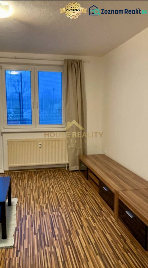 Prenájom 3 izbový byt, ulica Jána Poničana, BA IV. Devínska Nová Ves - Obývacia izba v 3-izbovom byte s podlahou s dreveným dekorom a výhľadom cez veľké okno.