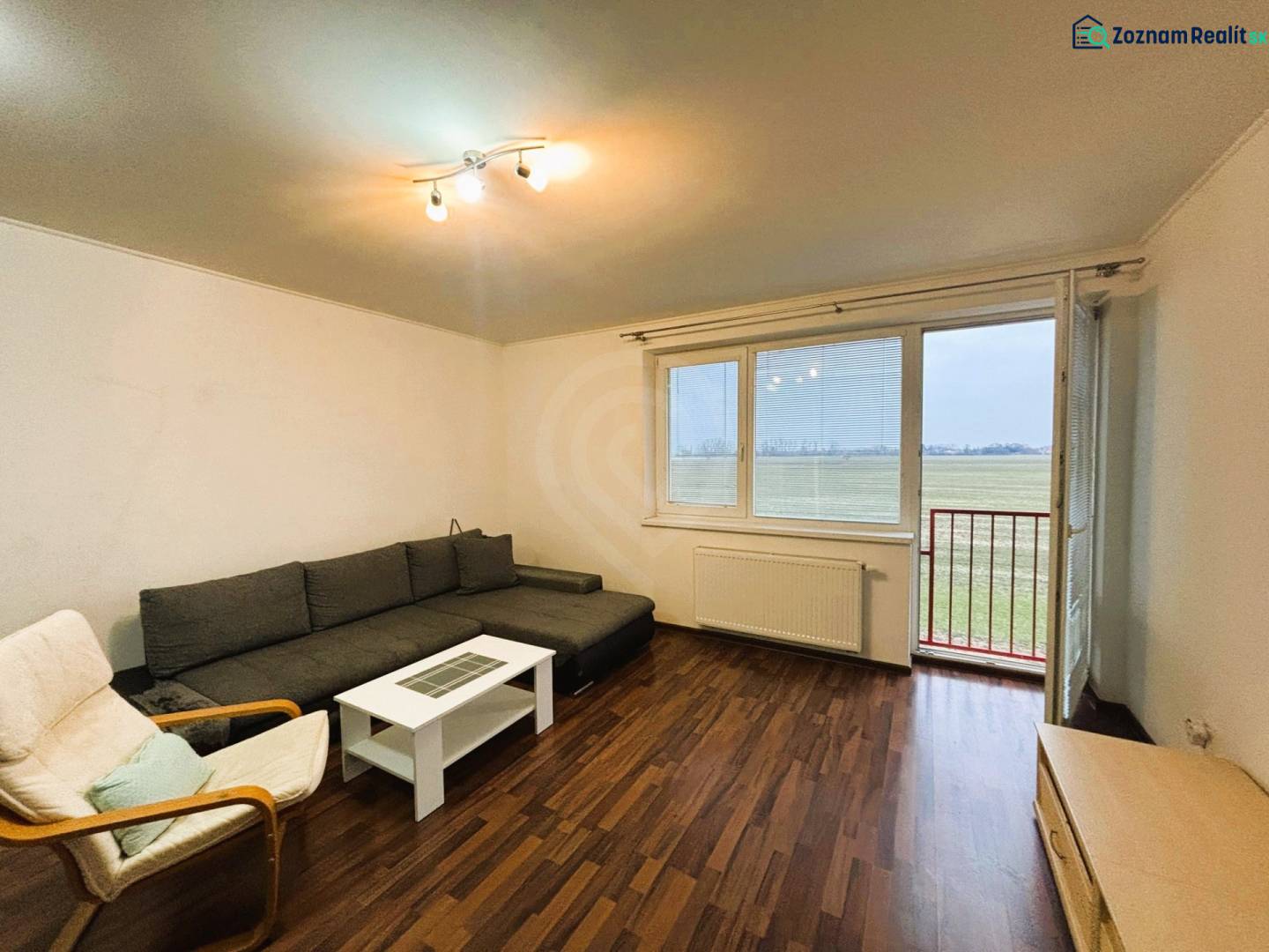 Prenájom 2 izbový byt – 52 m², lokalita – Malá Paka. - Obývacia izba v 2-izbovom byte s podlahou s dreveným dekorom a pohovkou.