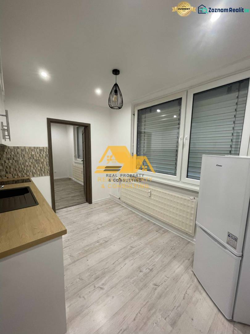 Prenajmem prerobený 1 izbový byt v Nových Zámkoch - Kuchyňa v 1-izbovom byte s podlahou s dreveným dekorom a bielymi elektrospotrebičmi.