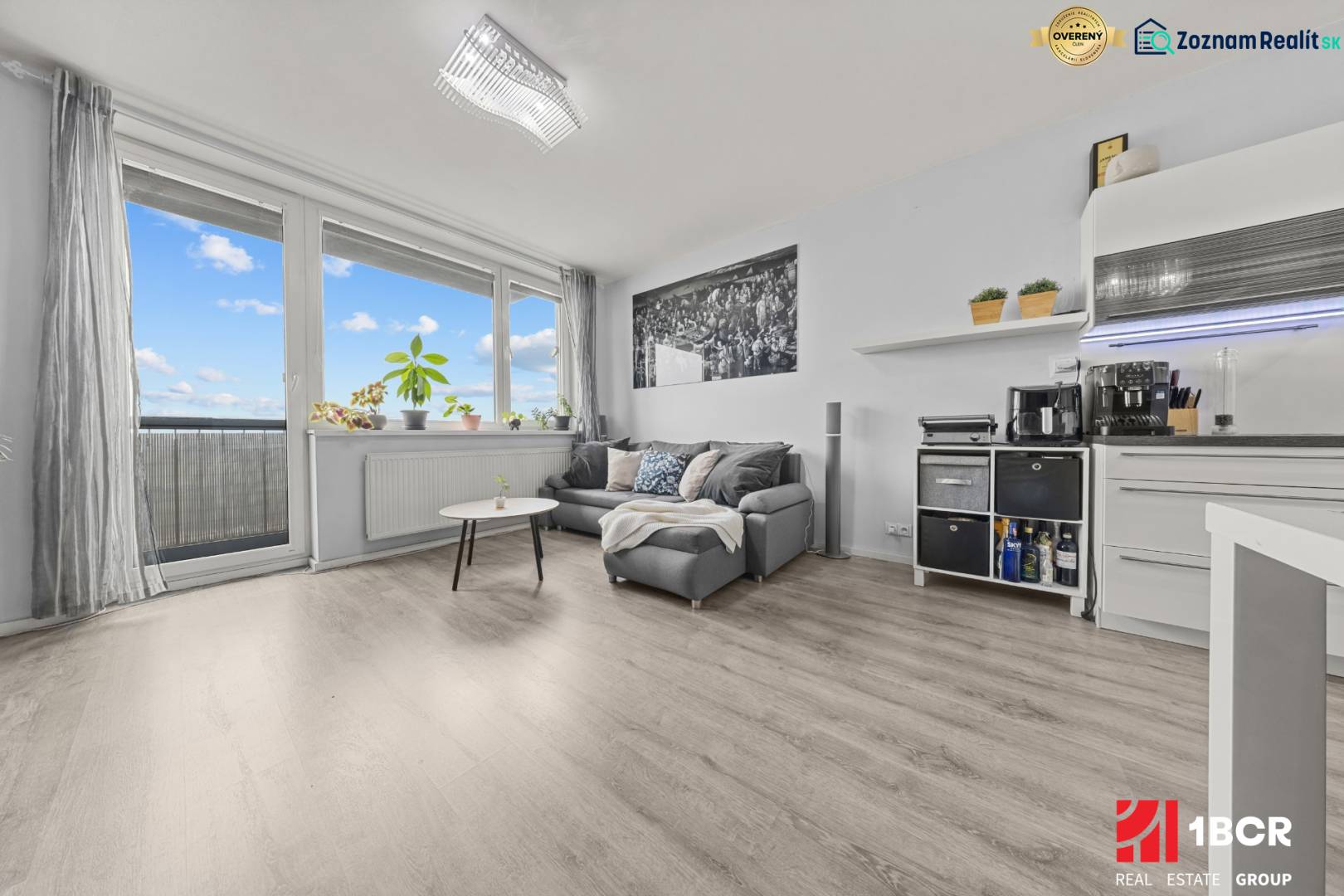 KOMPLETNE ZARIADENÝ 2-IZB. BYT,BALKÓN + PIVNICA,BUDATÍNSKA – PETRŽALKA - Obývacia časť 2-izbového bytu s pohovkou, stolíkom a podlahou s dreveným dekorom.