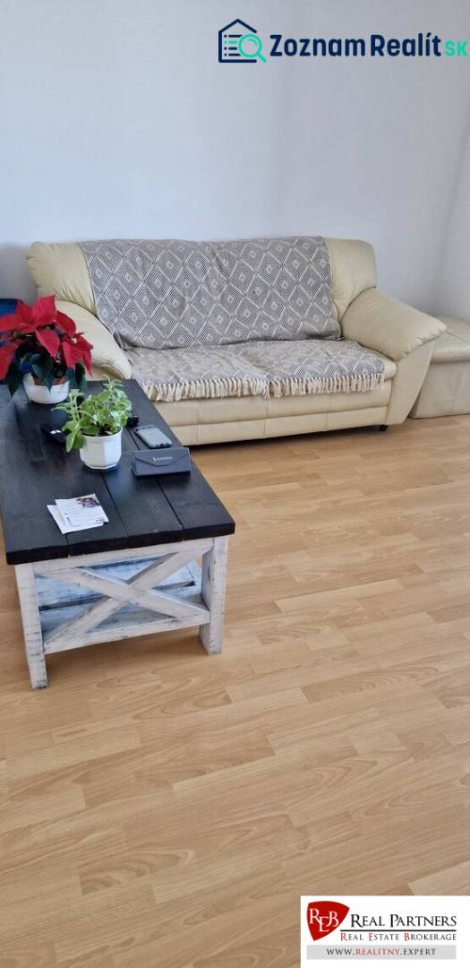 Prenájom 3 - izbový byt Bratislava - Petržalka - Pohovka a drevený stolík v 3-izbovom byte s podlahou s dreveným dekorom.