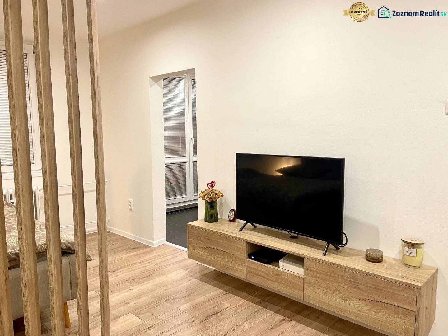 | Predaj 1-izbového bytu – Račianska, Bratislava - Izba s TV, podlahou s dreveným dekorom a stolíkom v 1-izbovom byte.