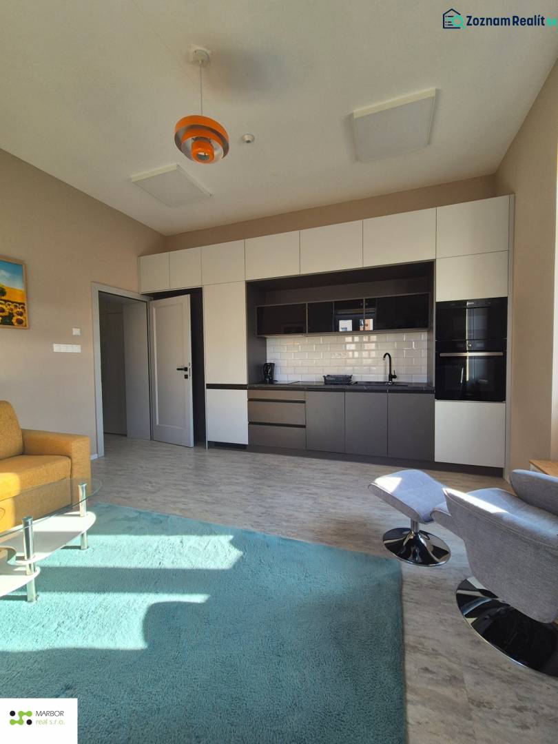 Na prenájom  plne zariadený apartmán na Južnej triede 44, Košice - Interiér 1-izbového bytu s kuchynskou linkou, zeleným kobercom a podlahou s dreveným dekorom.