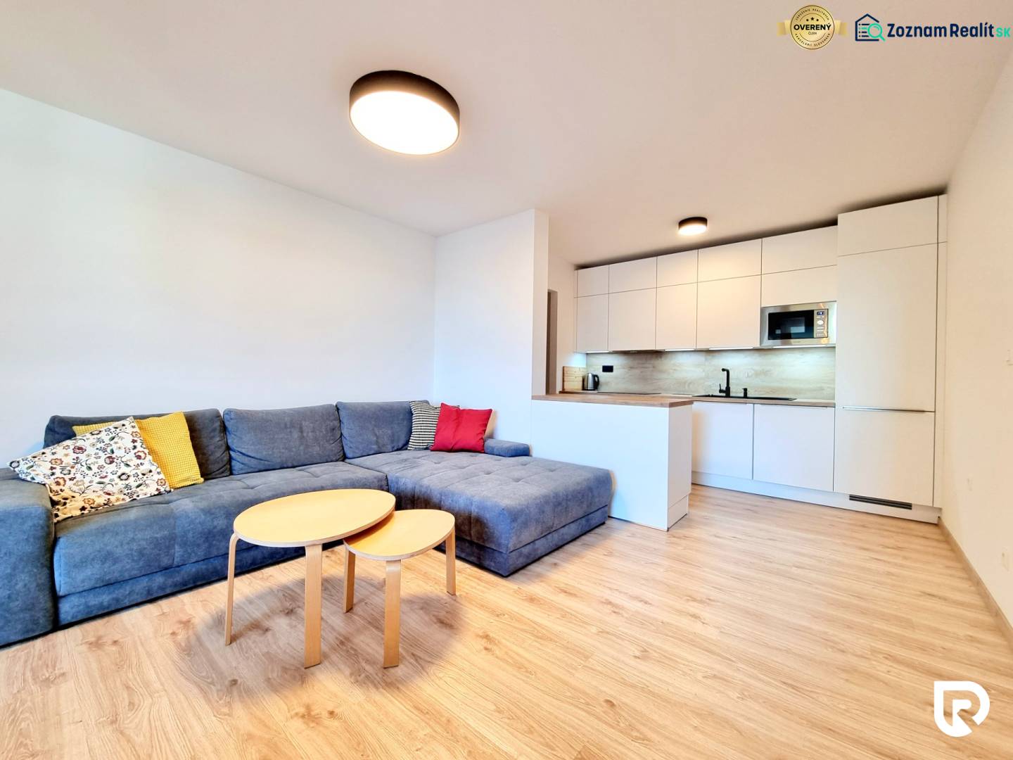 Pekný a moderný 3-izbový byt I Arboria Trnava - Obývacia izba s kuchyňou v 3-izbovom byte má podlahu s dreveným dekorom a rohovú sedačku.