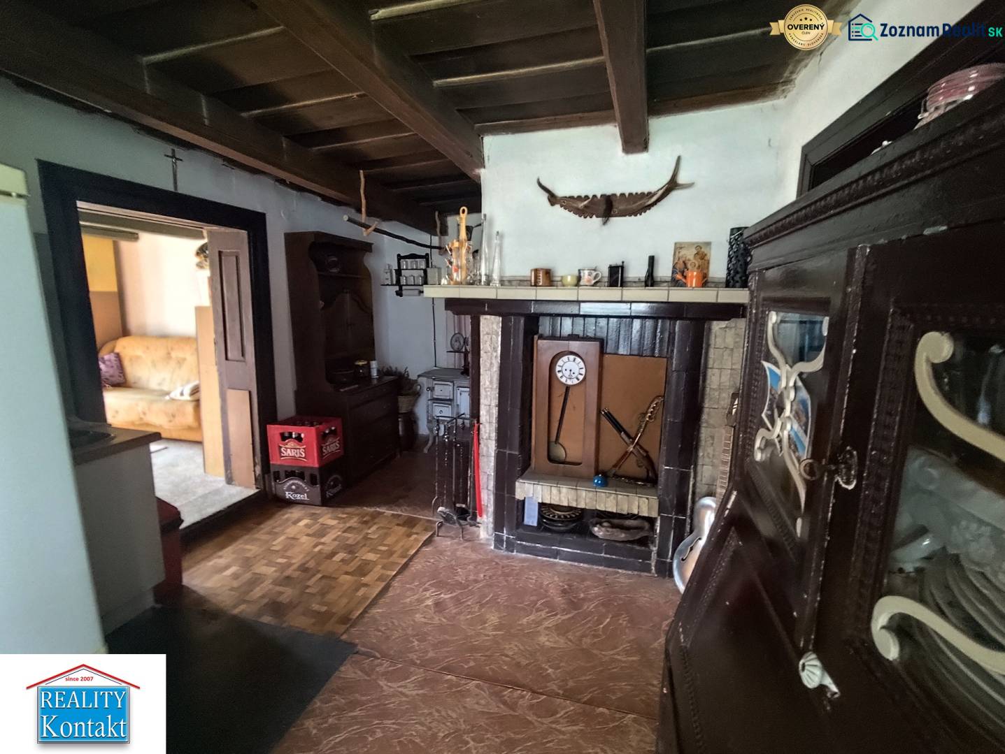 Ponúkame na predaj záhradný domček - Jasová - Interiér rodinného domu s kozubom, dekoratívnym riadom a otvorenými dverami do obývacej izby.