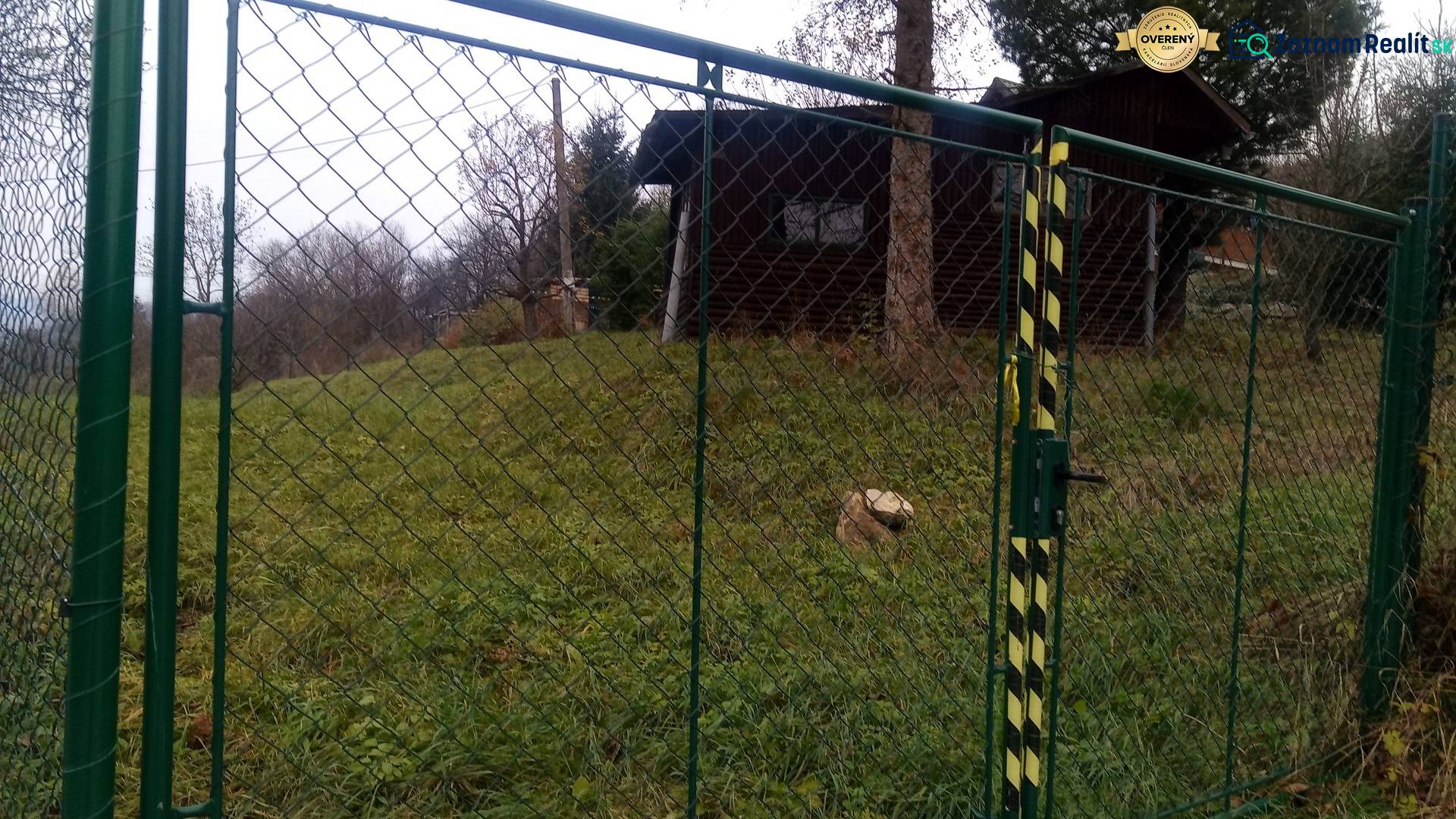 KONSKÉ - pozemok 1108 m2,okr. Martin  - Brána so zeleným pletivom, vedúca na trávnatý pozemok, blízko drevené obydlie.