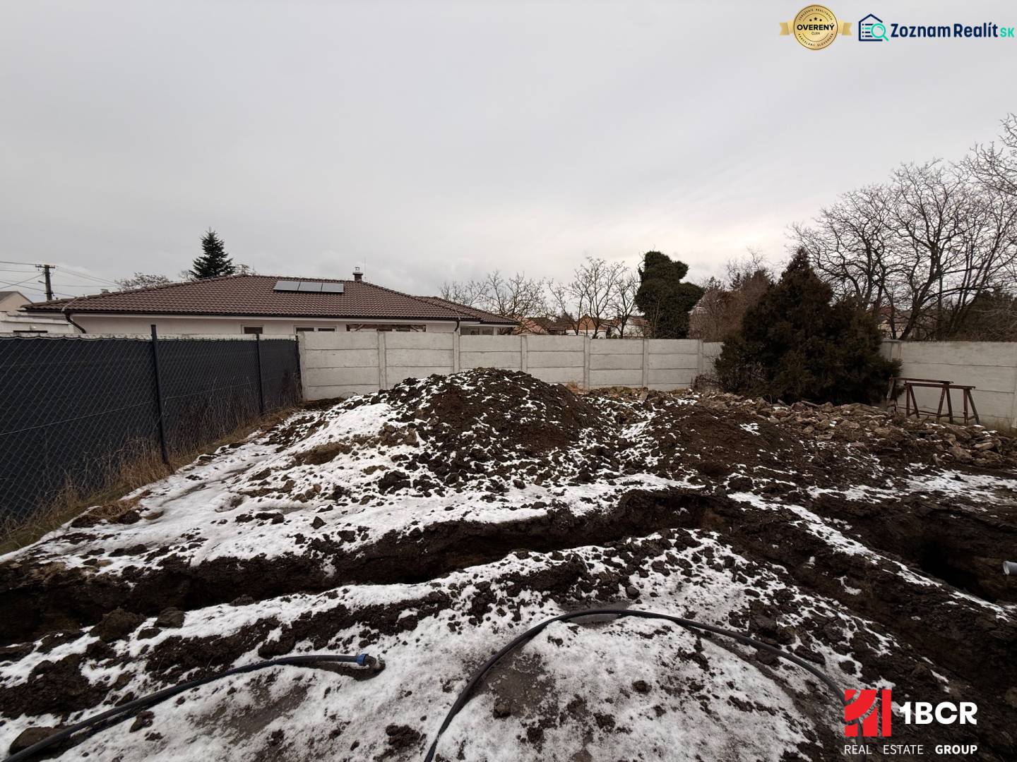 EXKLUZÍVNA SKOLAUDOVANÁ NOVOSTAVBA 4-IZB. RD Z KVALITNÝCH MATERIÁLOV - Stavenisko rodinného domu v Senci počas zimného obdobia s plotom a snehom.