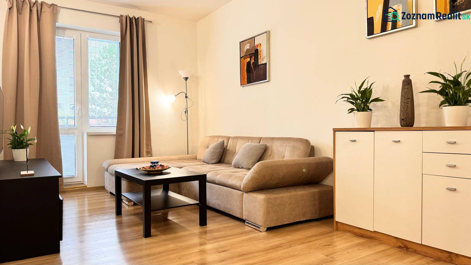 Prenájom 2 izbový byt Trenčín s vlastným parkovaním a terasou - Obývačka v 2-izbovom byte s béžovou sedačkou, podlaha s dreveným dekorom.