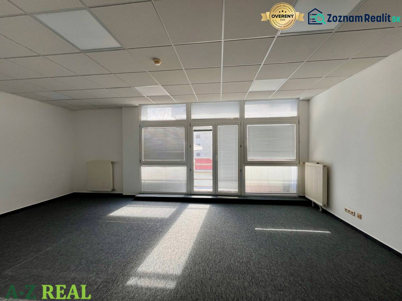 Prenájom kancelárskych priestorov 355 m2 ul. Stará Vajnorská - Kancelárie s veľkými oknami a sivým kobercom, biele steny, stropné osvetlenie.
