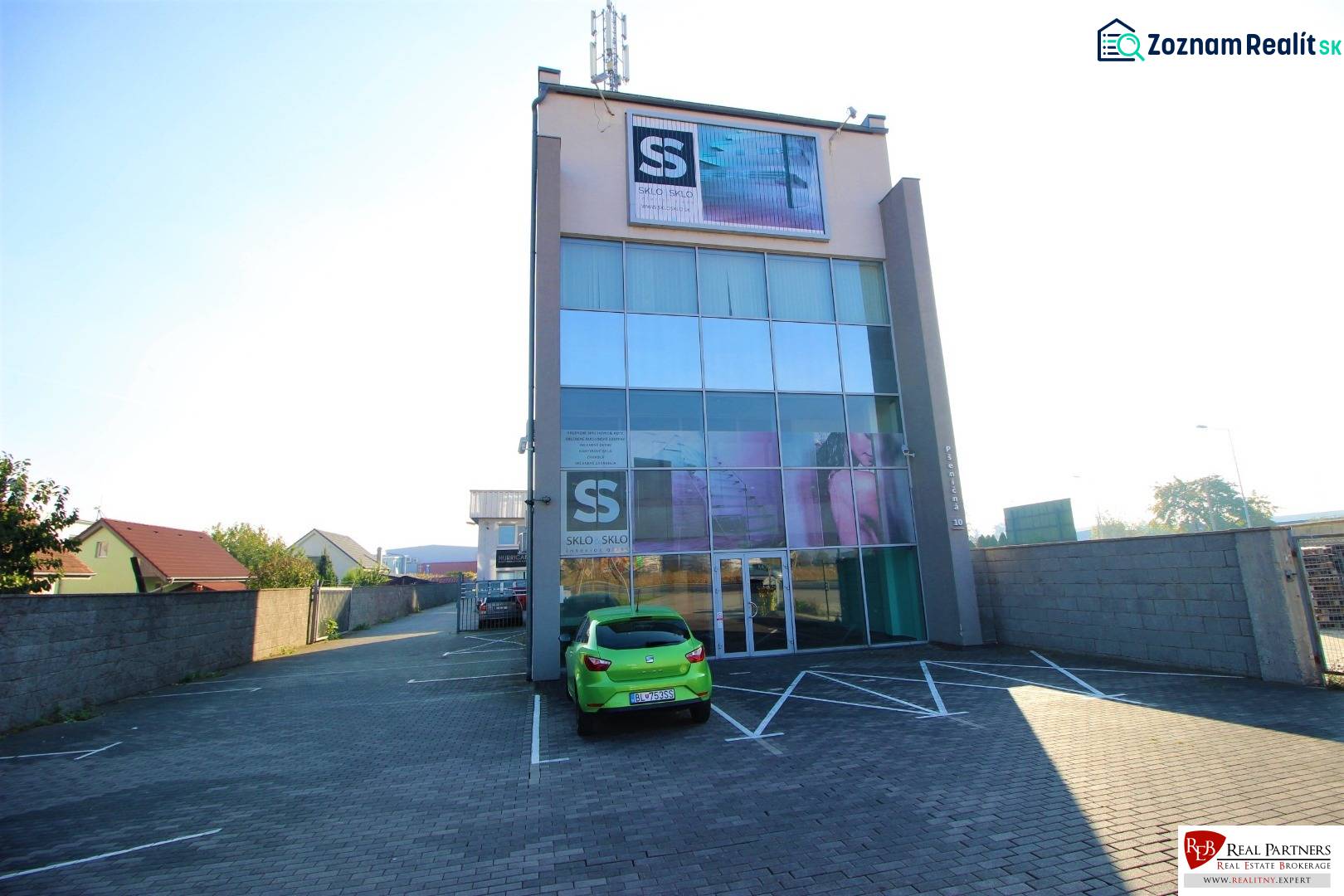 Predaj modernej administratívnej budovy v Bratislave, okres II - Štvorposchodová budova so sklenenou fasádou a parkoviskom pred vchodom.
