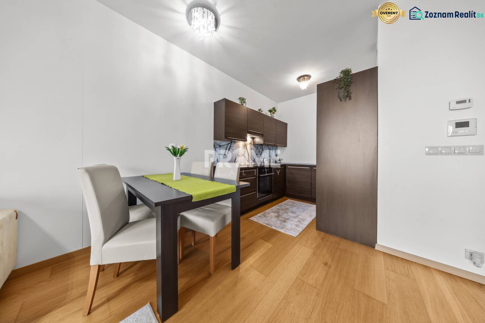 KRÁSNY 2i byt, KLÍMA, LOGGIA,VÝHĽAD,PANORAMA CITY, Landererova ulica - Jedálenský stôl a kuchyňa s tmavým nábytkom, podlaha s dreveným dekorom v 2-izbovom byte.