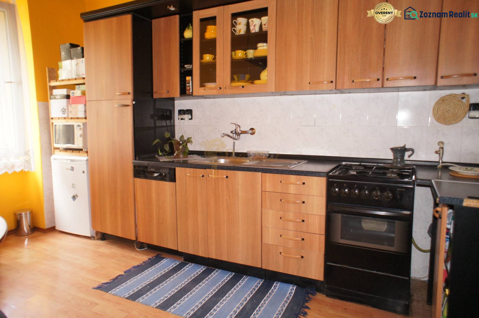 Veľký 1-izb. byt v tehlovom dome, Miletičova ul., Ružinov  - Kuchyňa s drevenou linkou, podlahou s dreveným dekorom, plynovým sporákom a chladničkou.
