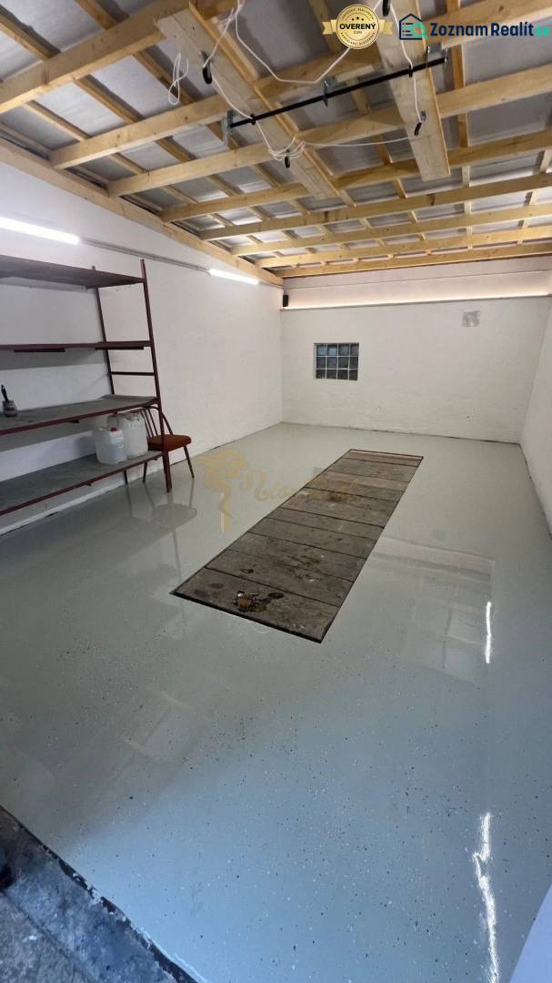 Zrekonštruovaná veľká garáž na ul. Agátova, Dúbravka s pozemkom - Garáže s regálmi a svetlými stenami, podlaha s jamou na opravu vozidiel.