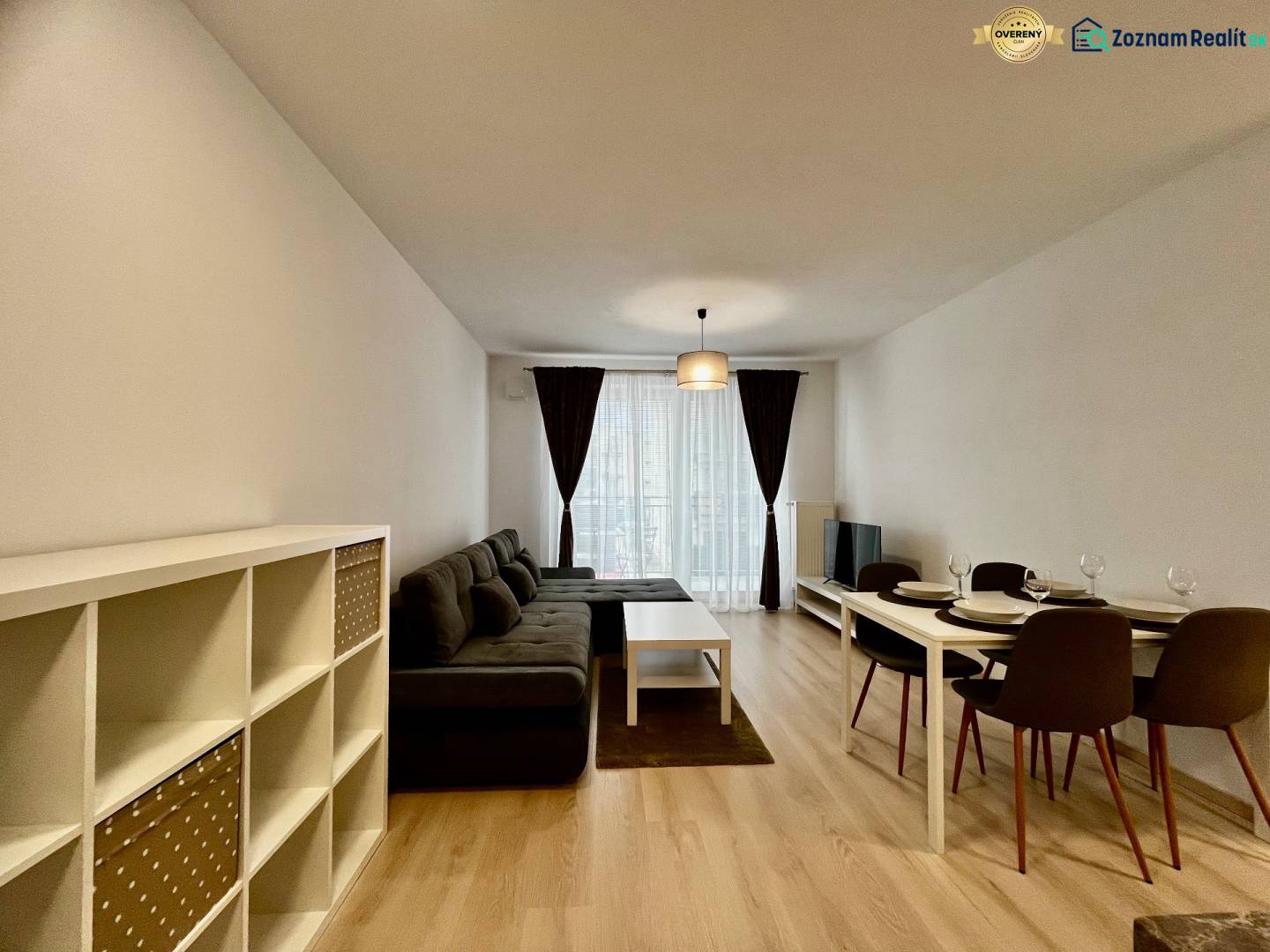 PRENÁJOM NOVOSTAVBA 2 izb.byt, BALKÓN, PARKOVACIE MIESTO, BIELY KOSTOL - Obývacia izba v 2-izbovom byte s pohovkou a jedálenským stolom, podlaha s dreveným dekorom.