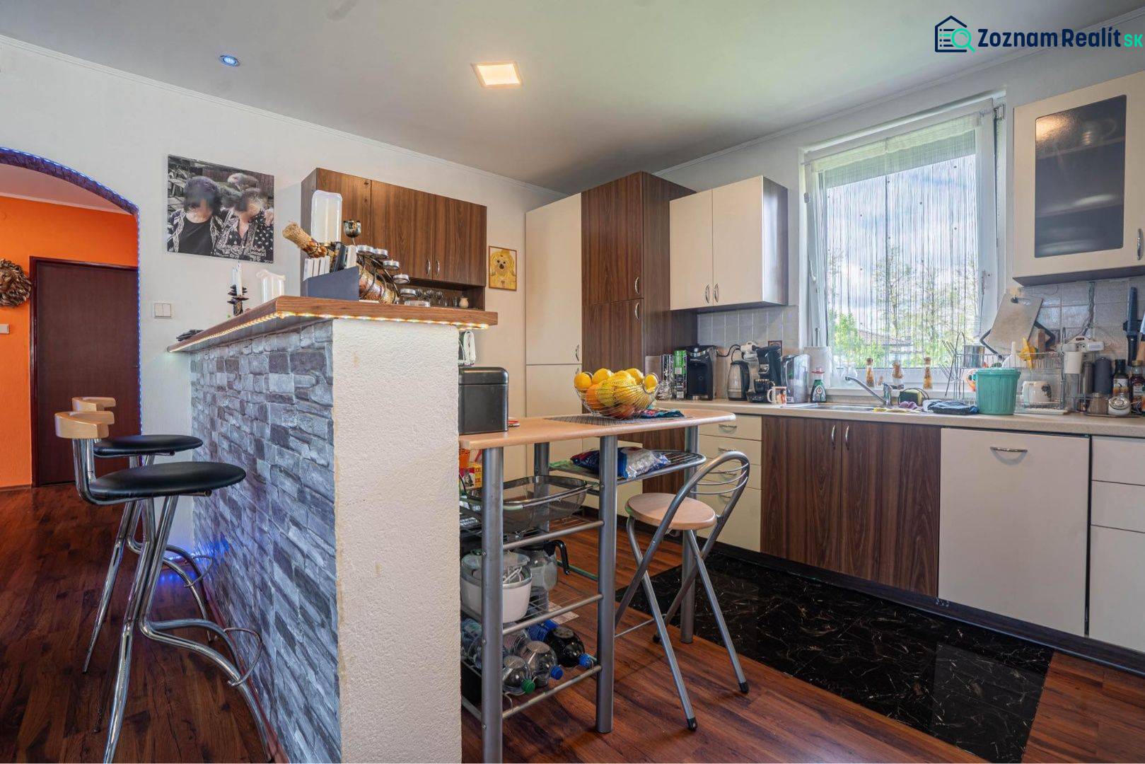 NA PREDAJ 3 IZBOVÝ RODINNÝ DOM, KĽÚČIAROVÉ KRAČANY - Kuchyňa v rodinnom dome s barovým pultom a podlahou s dreveným dekorom.