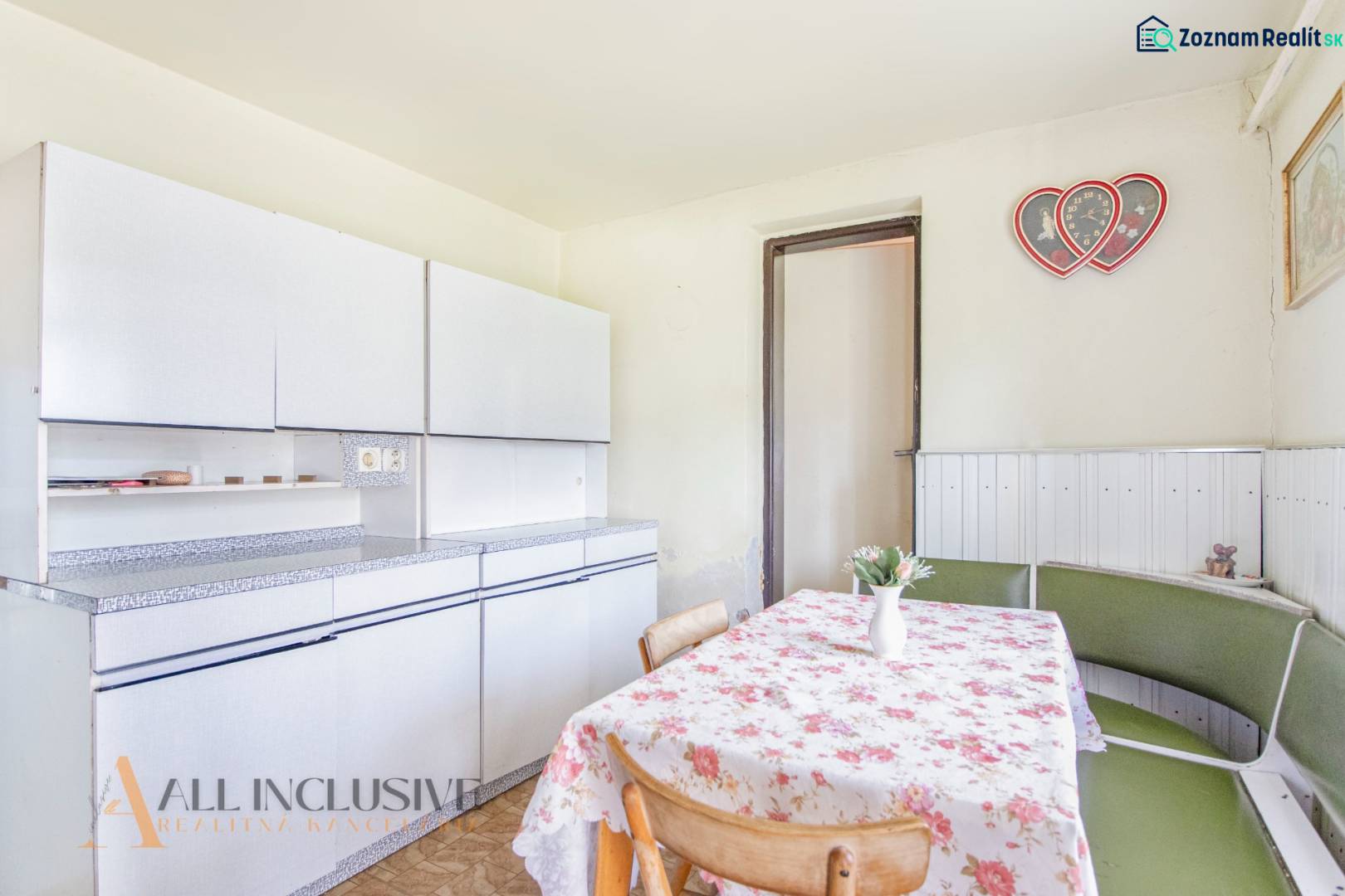 NA PREDAJ RODINNÝ DOM NA 9,5 ÁROVOM POZEMKU, OHRADY - Kuchyňa rodinného domu s bielymi skrinkami, kvetinovým obrusom a dekoráciou v tvare srdca.