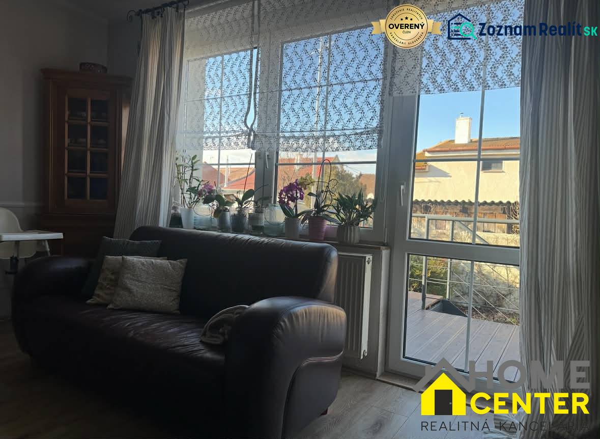 PREDAJ : RODINNÝ DOM, KOMÁRNO - Kožená sedačka a okno s čipkovanými závesmi v Rodinnom dome s podlahou s dreveným dekorom.