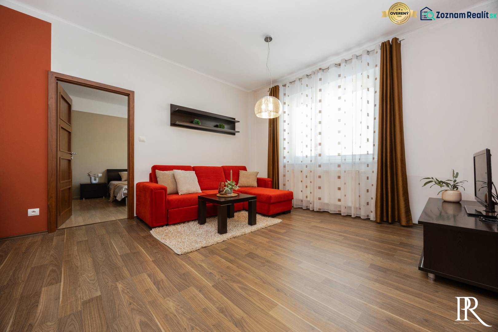 VEĽKÝ ZARIADENÝ 2IB PO KOMPLETNEJ REKONŠTRUKCII - Obývacia izba v 2-izbovom byte s červenou pohovkou a podlahou s dreveným dekorom.