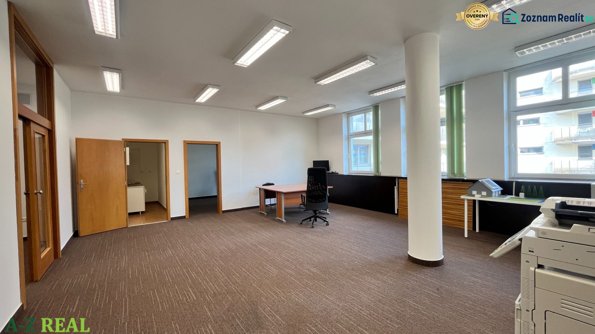 Prenájom kancelárskych priestorov s parkovaním v centre, 195m2  - Priestranná kancelária so stolmi, kancelárskymi stoličkami a veľkými oknami, poskytujúca dostatok svetla.