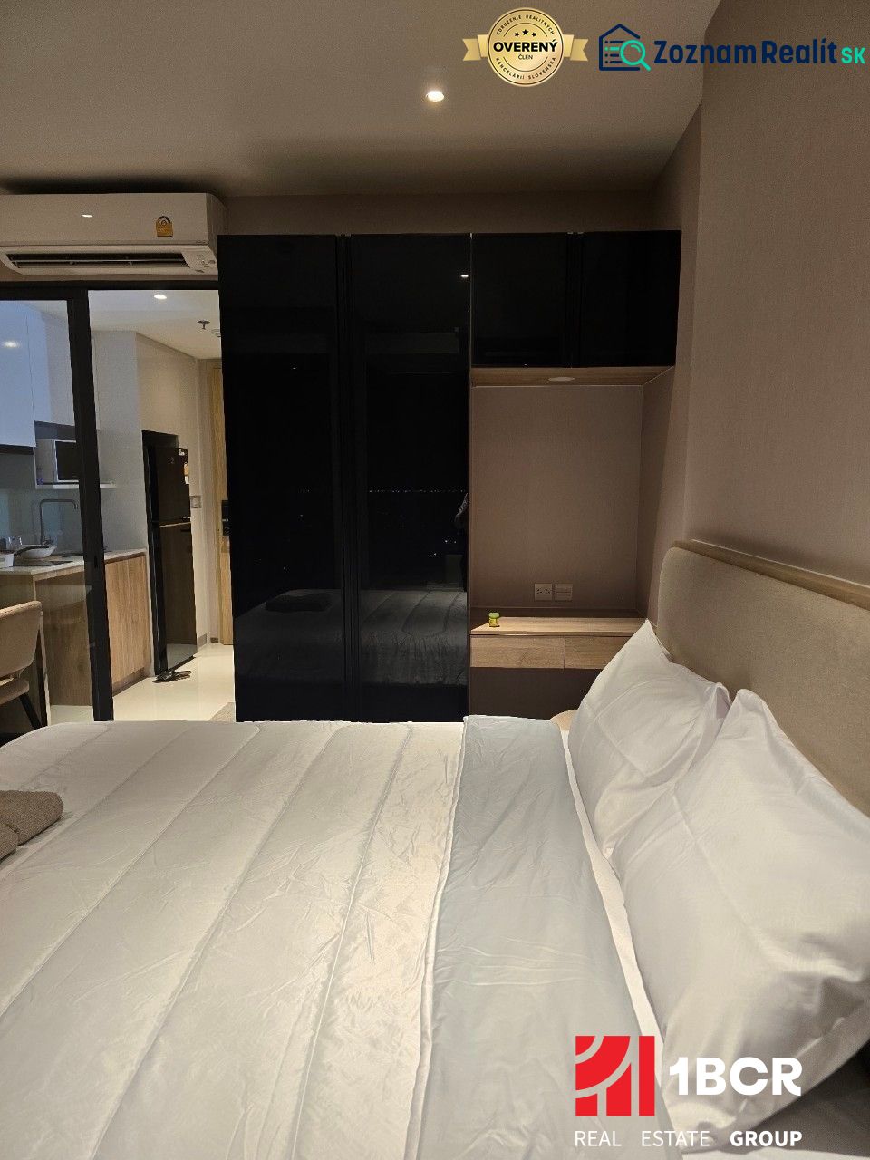 ŠTÚDIO ONCE PATTAYA - Spálňa s bielou posteľou a čiernou skriňou, vedľa kuchynskej linky.