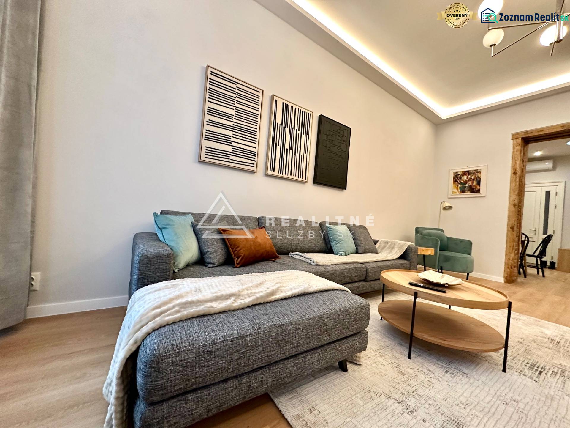 Prenájom priestranného 2-izbového bytu v absolútnom centre Košíc - Obývacia izba s pohovkou, podlahou s dreveným dekorom a umeleckými dielami v 2-izbovom byte.