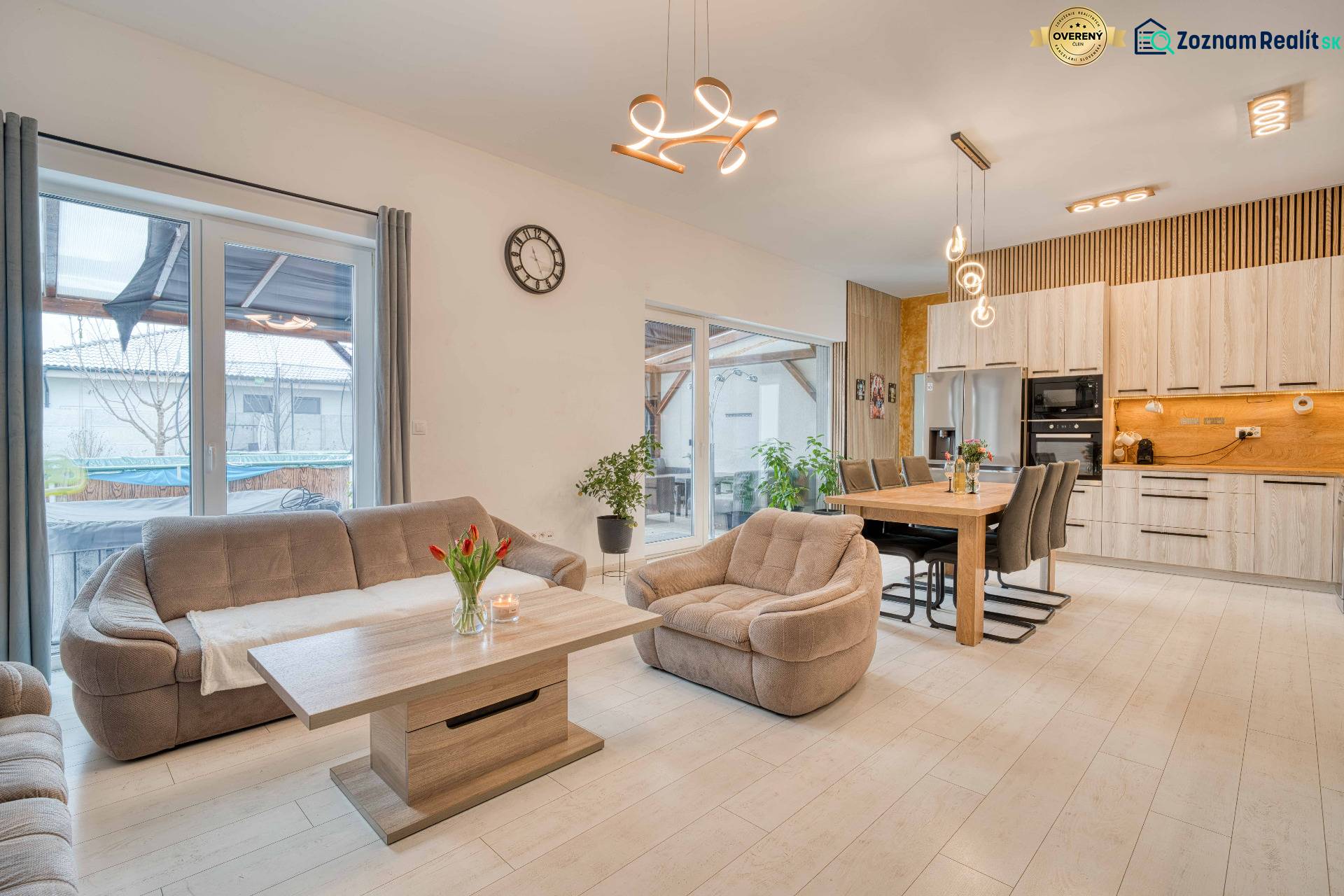 Unikátna 4i NOVOSTAVBA, Špačince 740m² pozemok len pár minút od Trnavy - Obývačka spojená s kuchyňou, pohovka, stôl, svetlá a podlaha s dreveným dekorom.