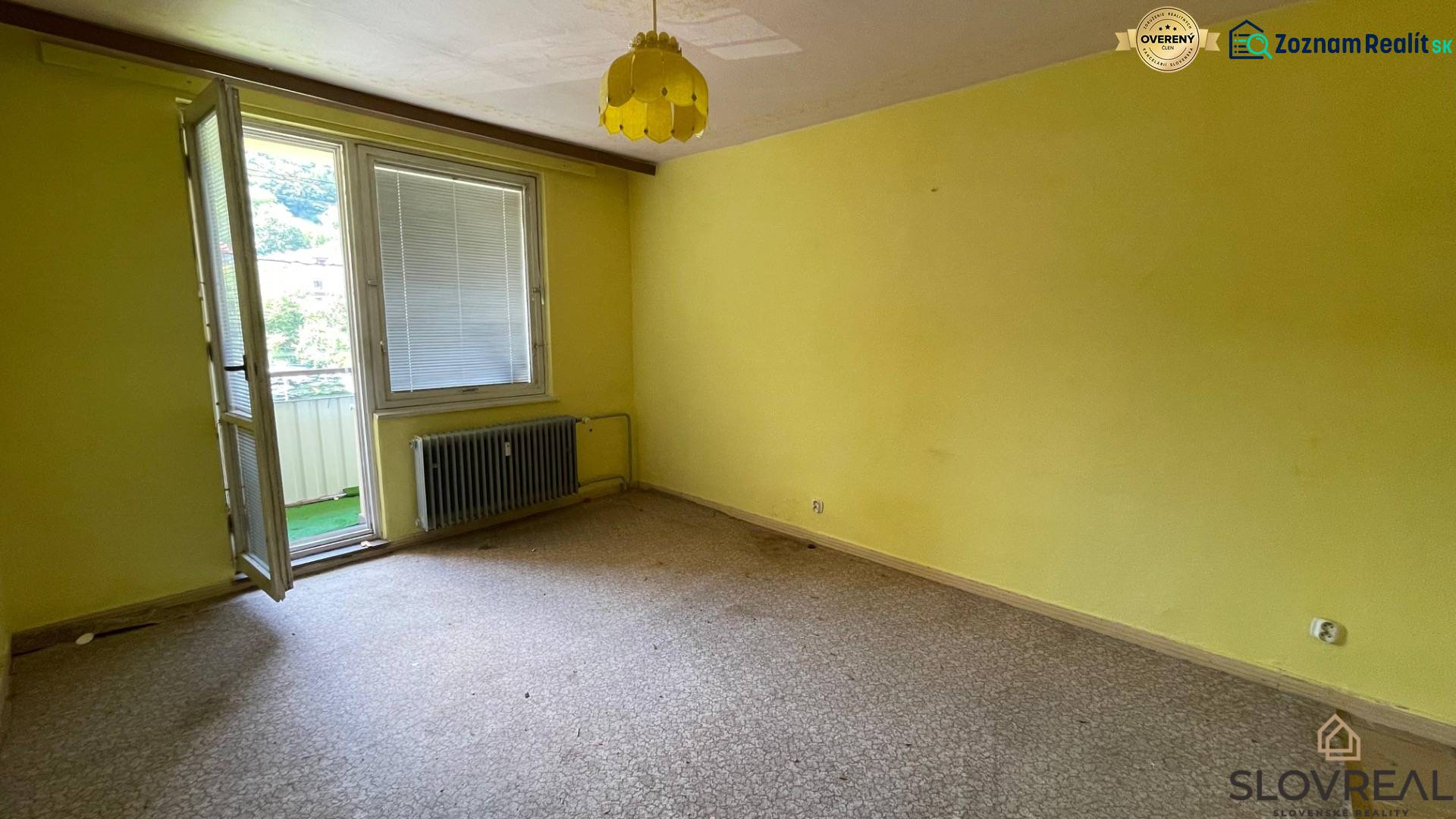 Na predaj veľký 3-izbový byt s lodžiou v Detve - Novosady - Izba v 3-izbovom byte so žltými stenami, otvoreným balkónom a radiátorom.