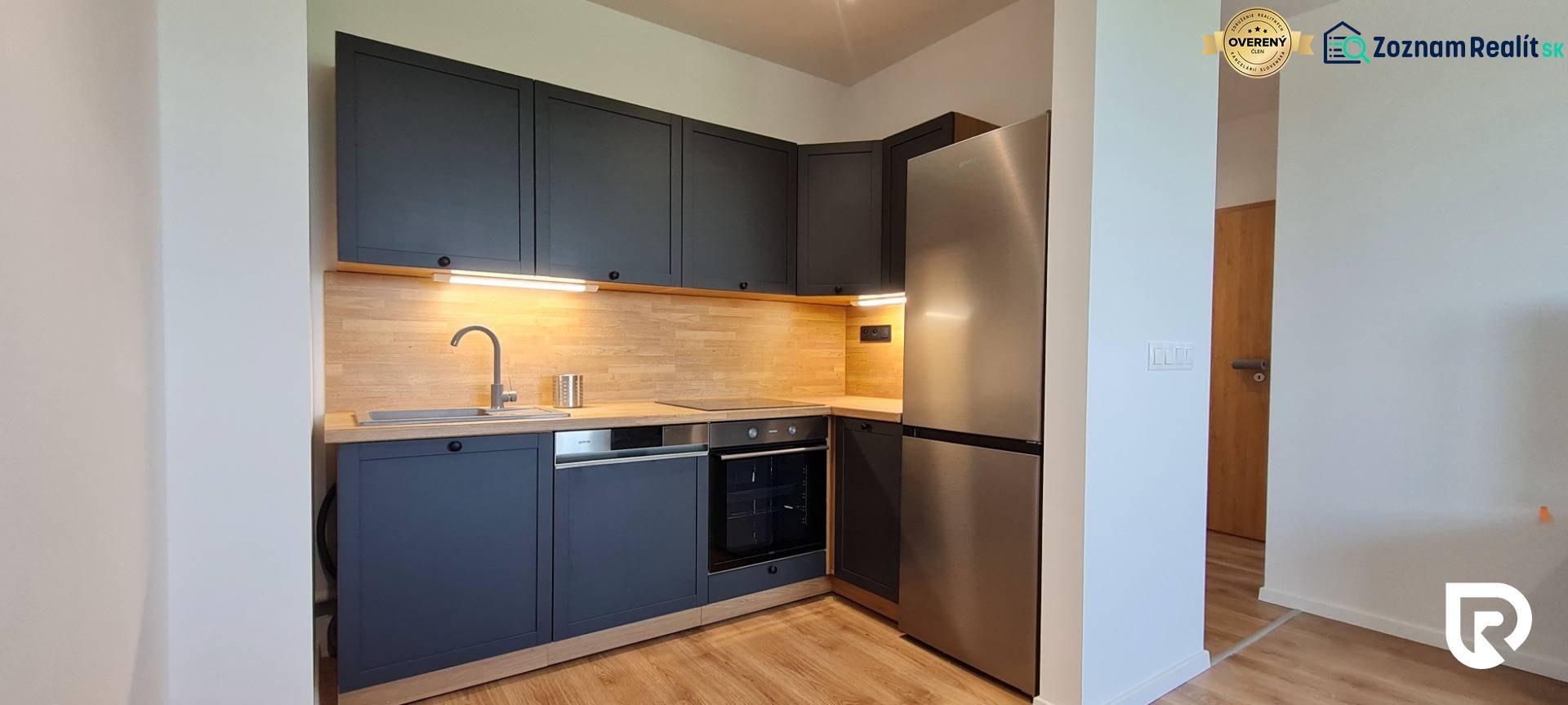 Zariadený 2-izb. byt v novostavbe v Ružinove - Ovocné sady - Kuchyňa v 2-izbovom byte s tmavosivými skrinkami, dreveným dekorom a nerezovými spotrebičmi.