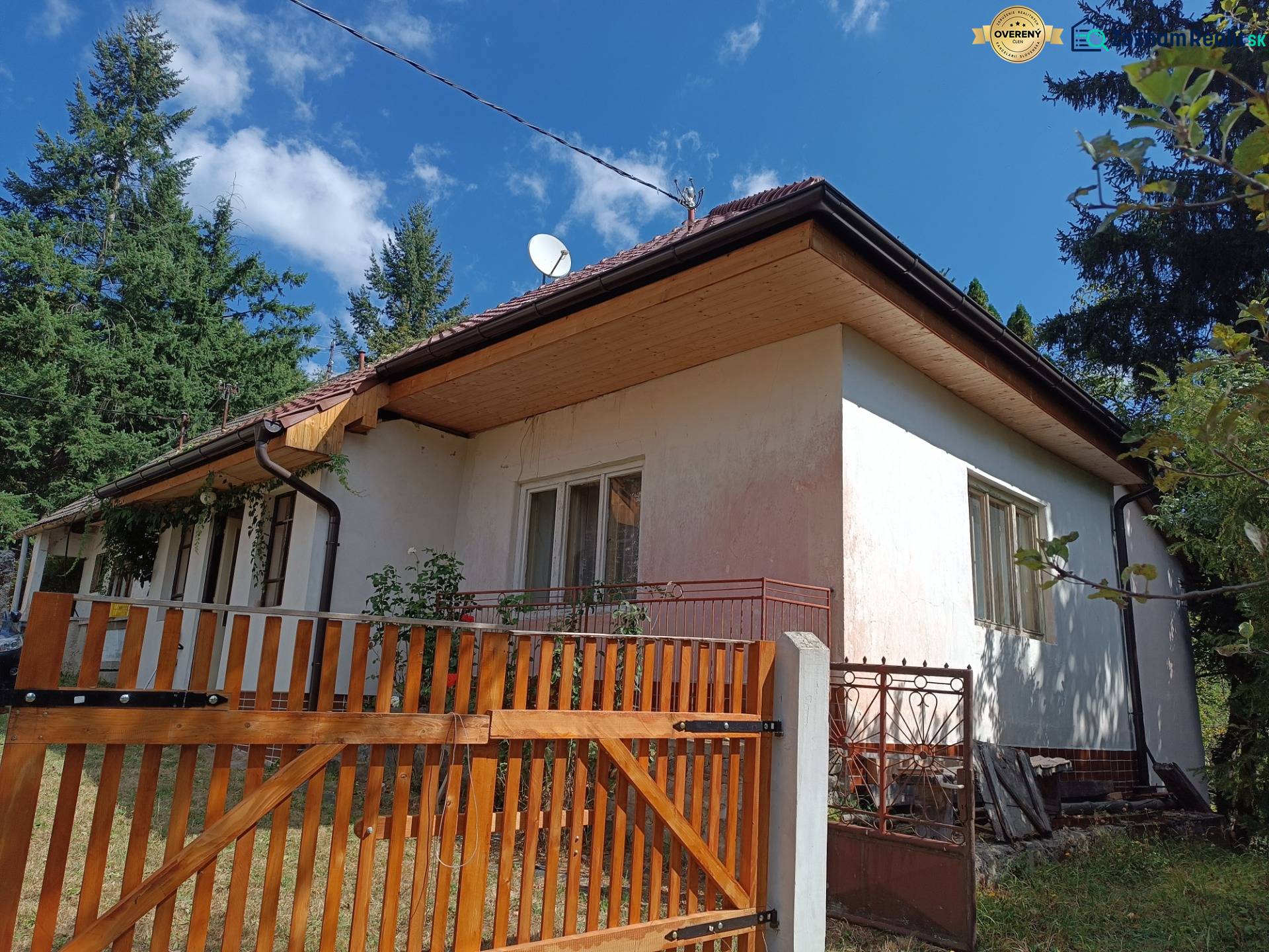 Hospodárska usadlosť s 3,6 hektárovým pozemkom na samote Nová Baňa - Tradičný rodinný dom s dreveným plotom uprostred krásnej prírody a oblohy plnej oblakov.