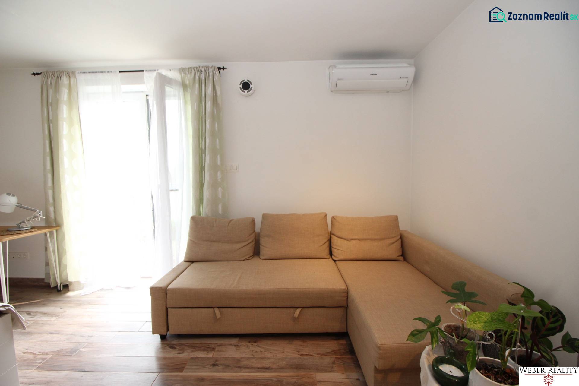 1-izb. kompletne zrekonštr.byt na Hradnom kopci (Lichardova ul.)  - Světlo z okna v 1-izbovom byte so sedačkou, pracovným stolom a podlahou s dreveným dekorom.