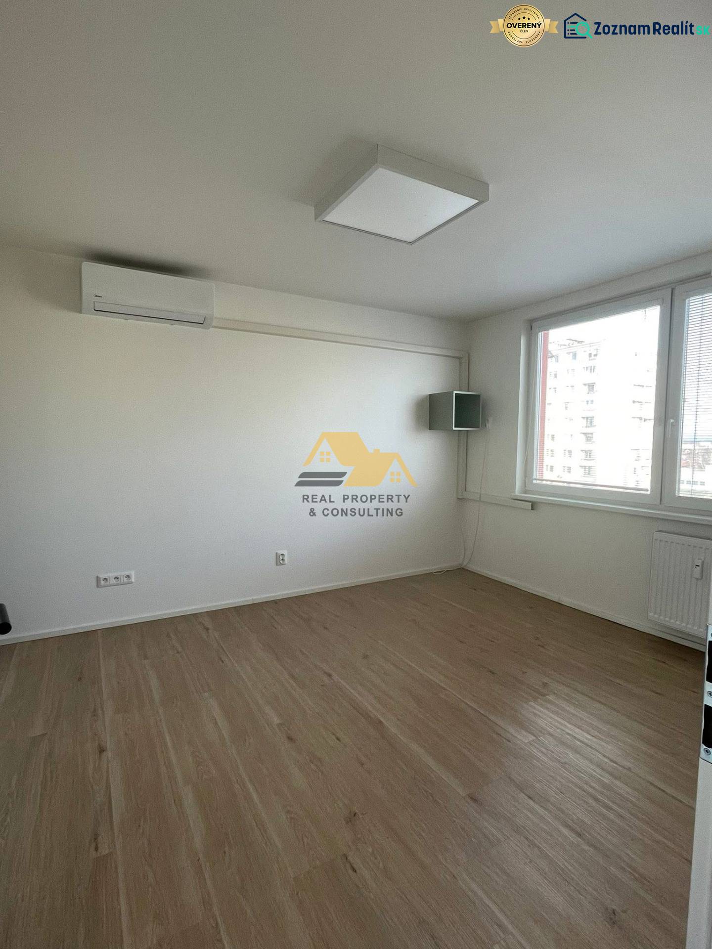 Prenajmem 1 izbový byt na Nábrežnej ulici v Nových Zámkoch - Izba s bielymi stenami a podlahou s dreveným dekorom v 1-izbovom byte.