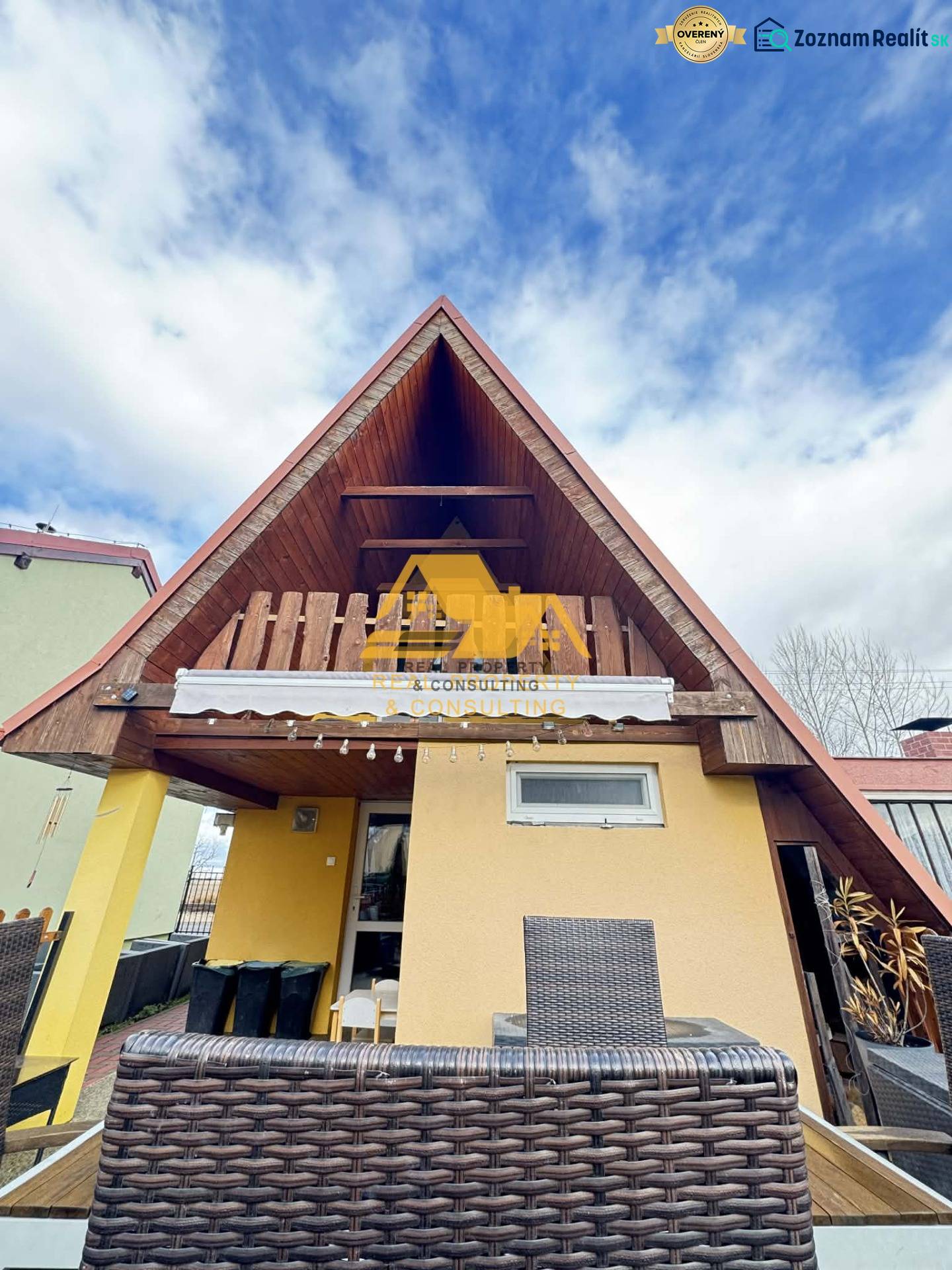 Predám peknú chatu na celoročné bývanie v Nových zámkoch - Drevená chata s terasou v Nových Zámkoch pod modrým oblohou.