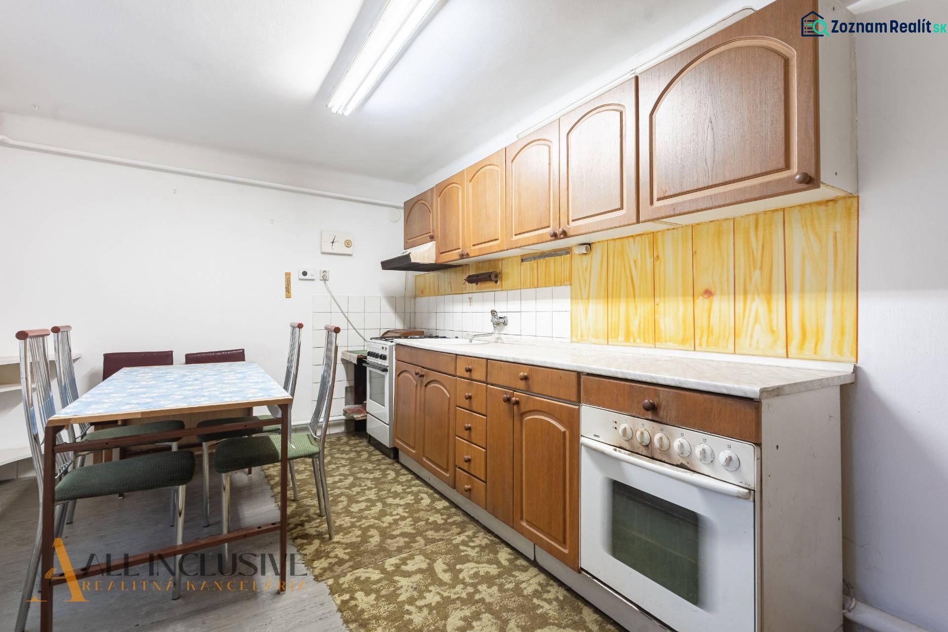 Na predaj 4-izbový rodinný dom, Gabčíkovo - Kuchyňa v rodinnom dome s drevenými skrinkami a kobercom pri jedálenskom stole.