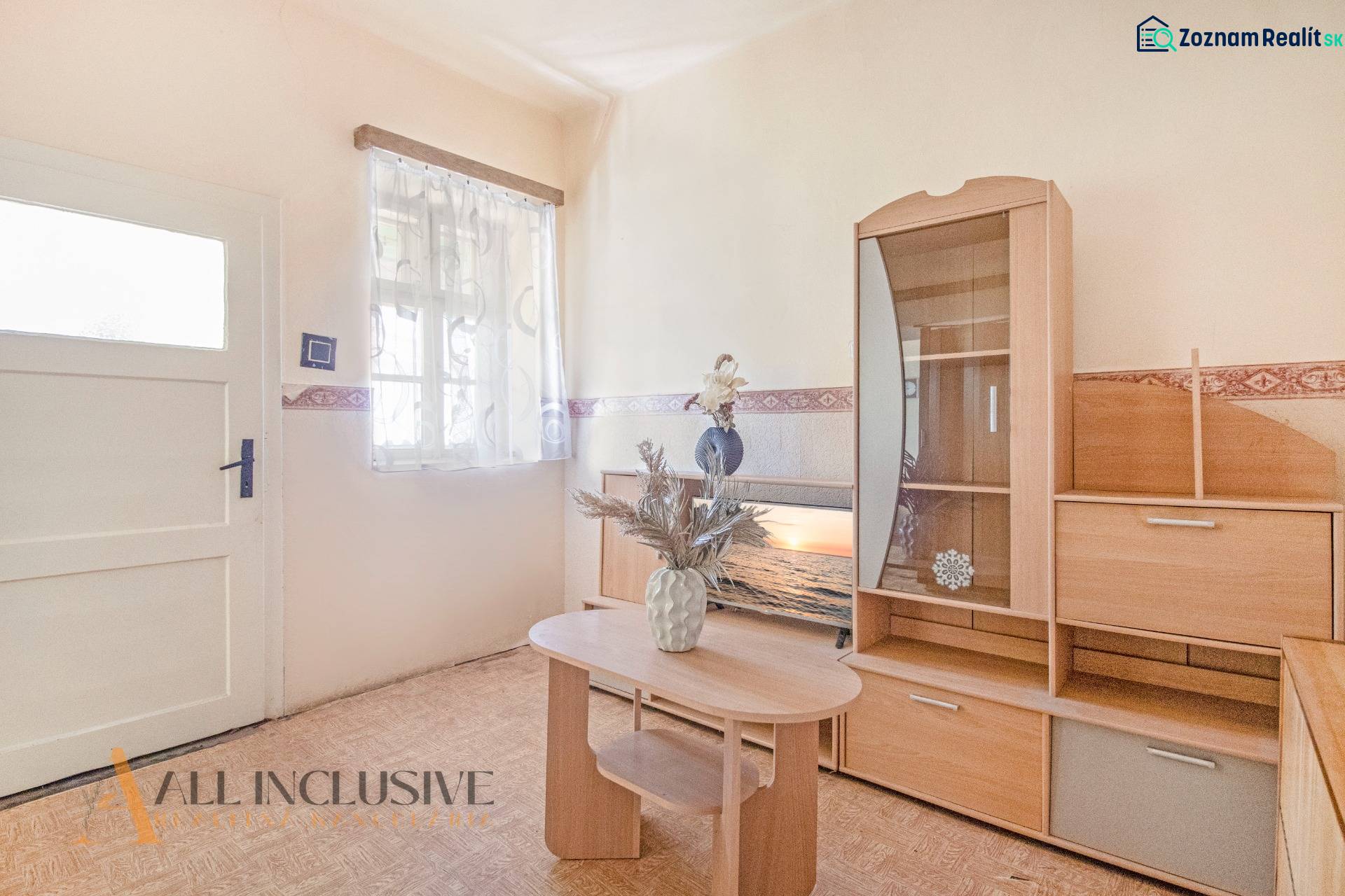 NA PREDAJ 4-IZBOVÝ RODINNÝ DOM NA PRIESTRANNOM POZEMKU - Obývacia izba rodinného domu s dreveným nábytkom a dekoratívnou vázou na stole.