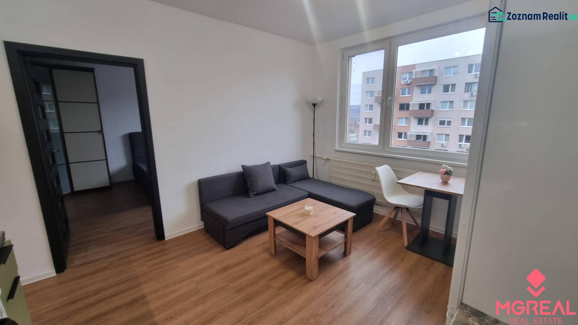 Prenájom 1- izbový byt  - Obývacia izba v 1-izbovom byte s pohovkou, stolom, stoličkou a podlahou s dreveným dekorom.