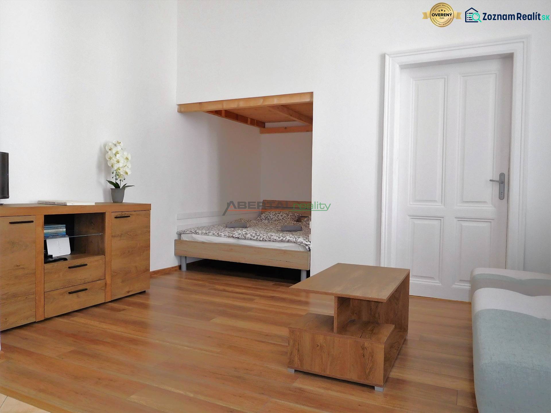 Predaj - štýlový 2i byt  v srdci Starého Mesta - Marianska, BA - Obývacia izba 2-izbového bytu s posteľou, skrinkou a podlahou s dreveným dekorom.