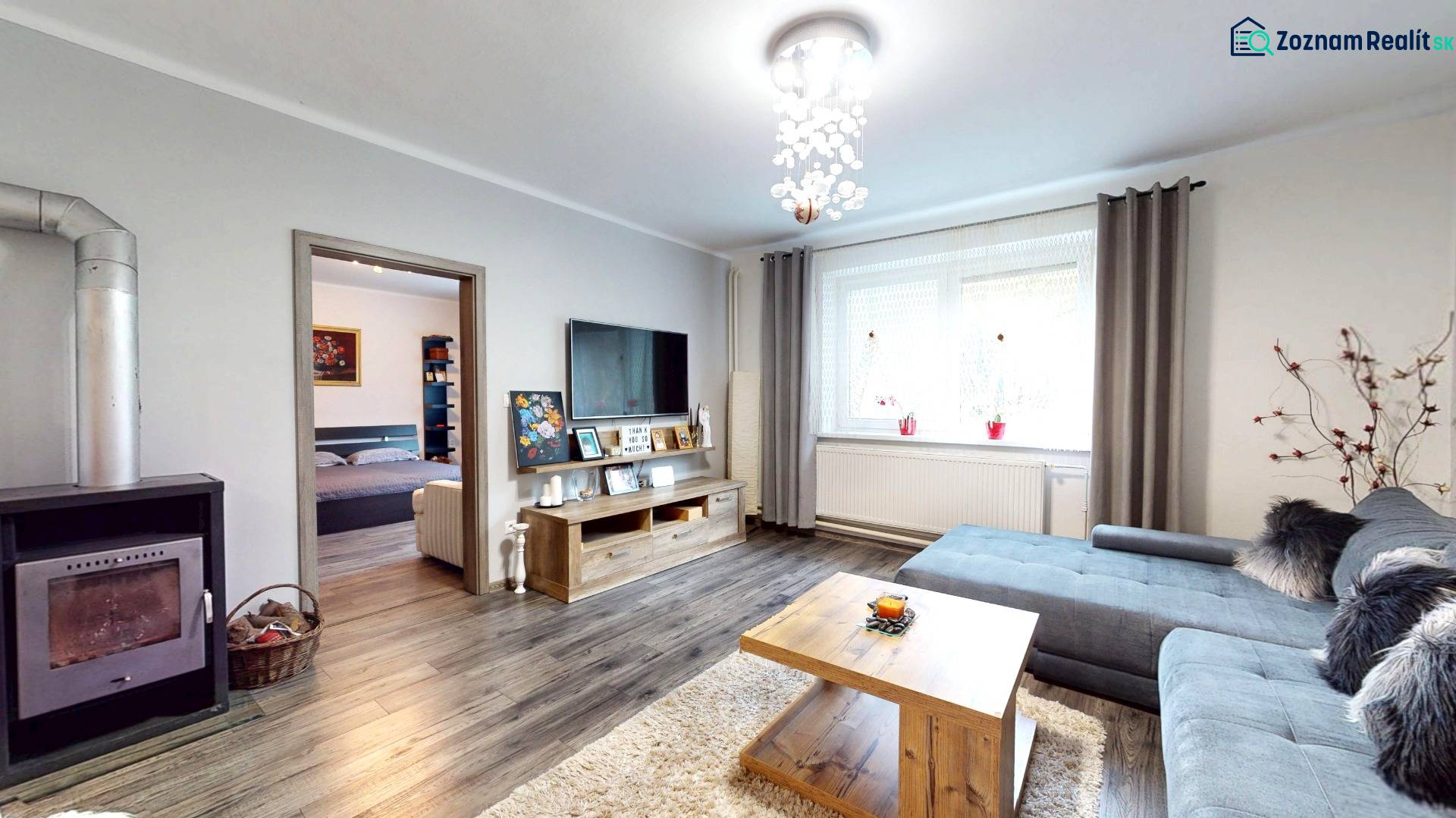 Prerobený rodinný dom na veľkom tichom pozemku v obci Pruské   - Obývacia izba v rodinnom dome s kozubom, podlahou s dreveným dekorom a sedacou súpravou.