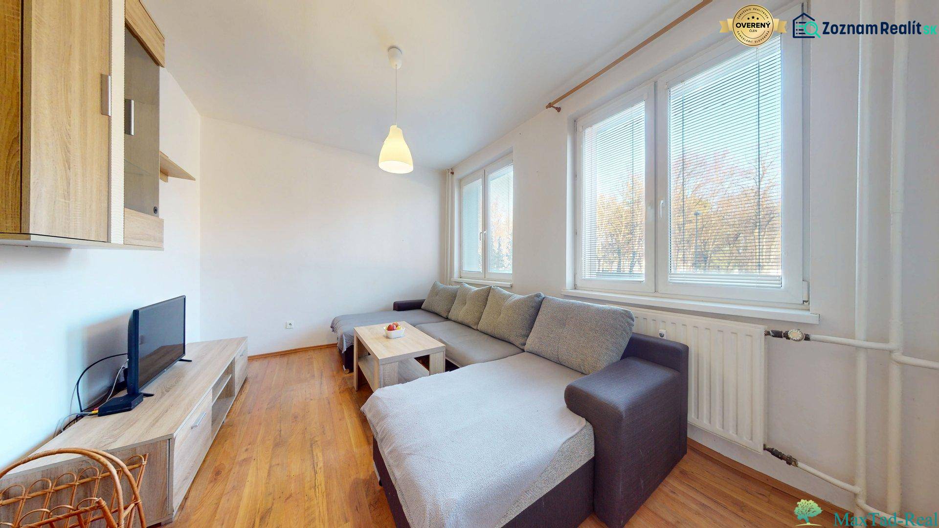 3-izbový byt s extrémne nízkymi nákladmi v Michalovciach - Obývacia izba v 3-izbovom byte s pohovkou, TV a podlahou s dreveným dekorom.