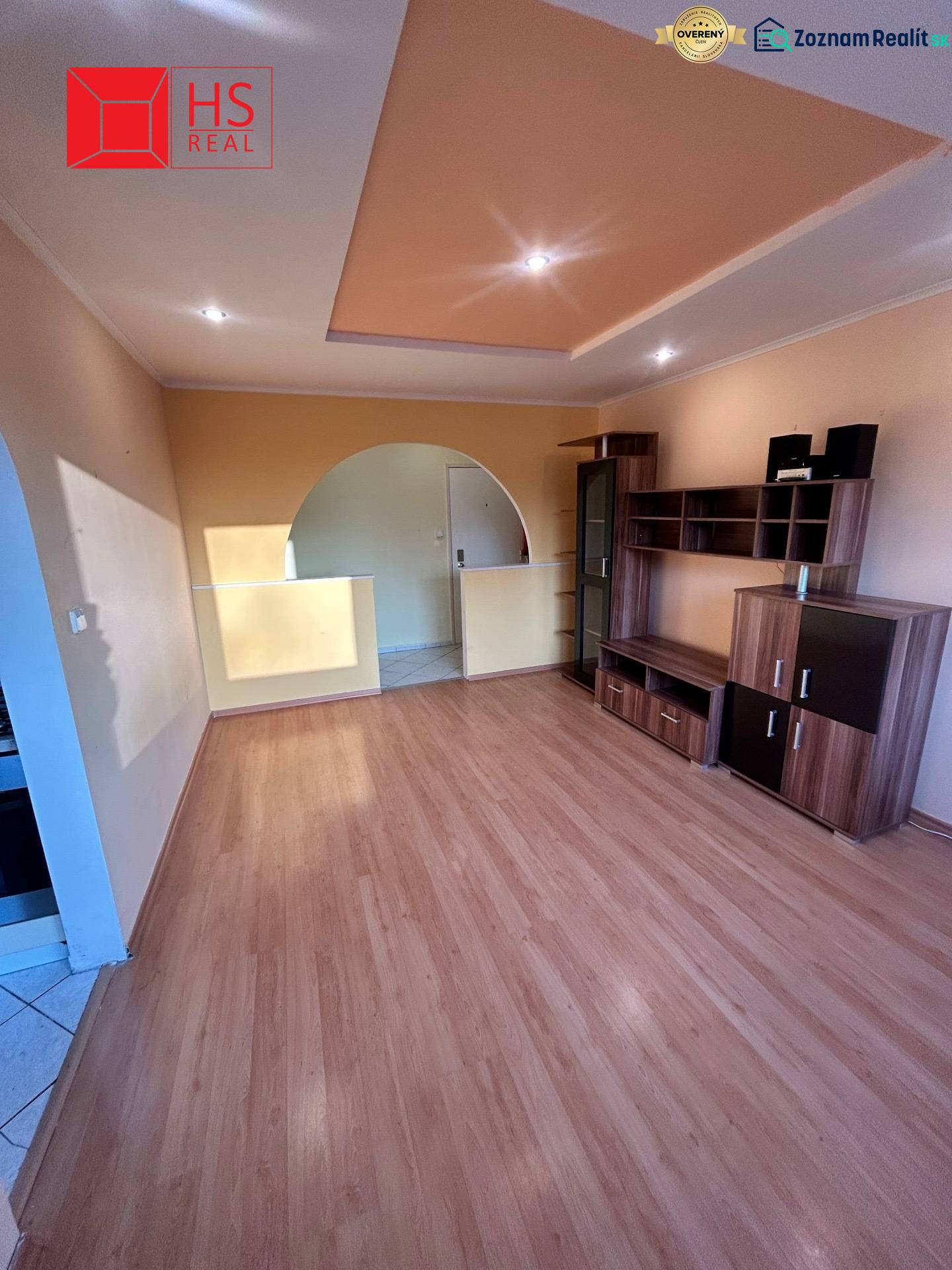 Predaj 3 izb. bytu s balkónom v NZ - Obývacia izba v 3-izbovom byte s podlahou s dreveným dekorom a vstavaným osvetlením.