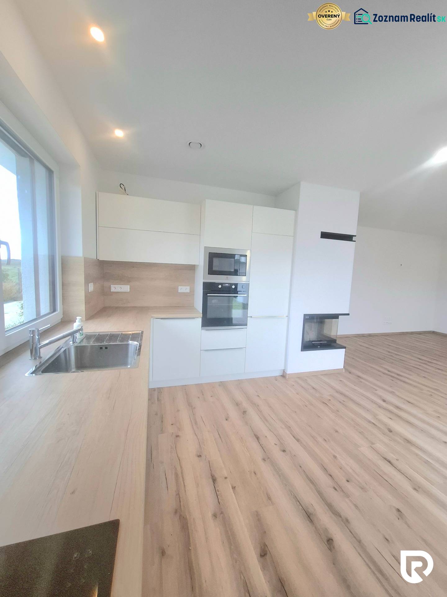 | 4 izbový rodinný dom s krbom a terasov | Slnečná | Ružindol - Biela kuchyňa s dreveným dekorom a vstavaným krbom v rodinnom dome.