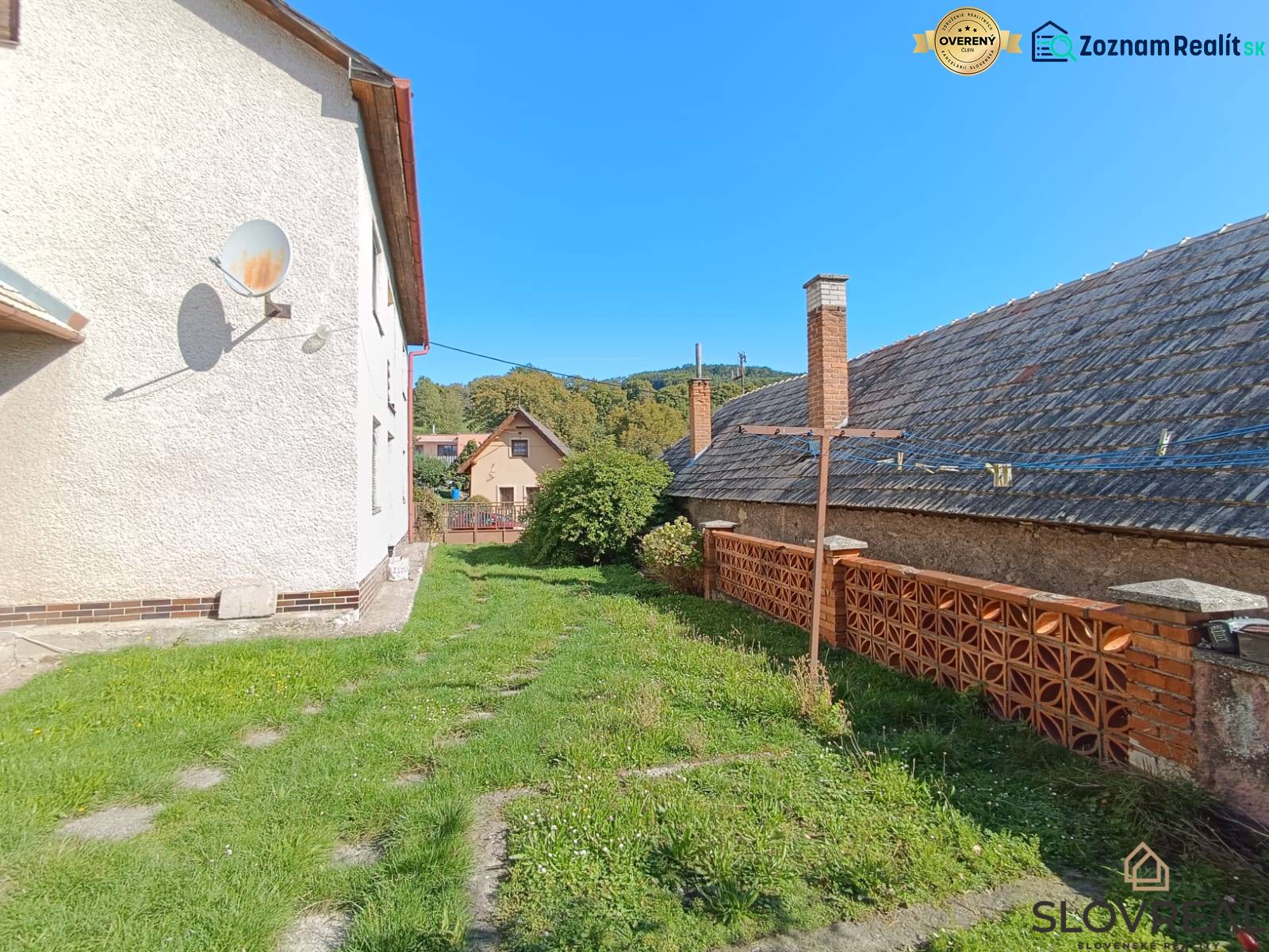 : Predaj rodinného domu s veľkým pozemkom v obci Pitelová  - Exteriér rodinného domu v Pitelovej so satelitom, trávnikom a tehlovým plotom.