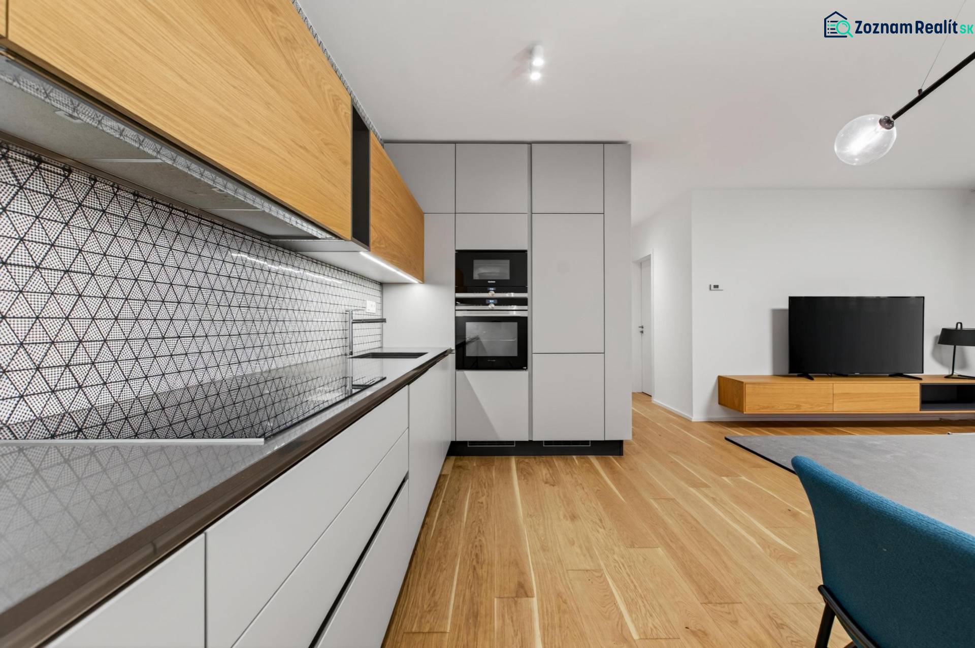 ︱ PREDAJ Nadštandardný 3-izb. byt v projekte Gansberg Koliba - Kuchyňa v 3-izbovom byte s geometrickým obkladom a podlahou s dreveným dekorom.