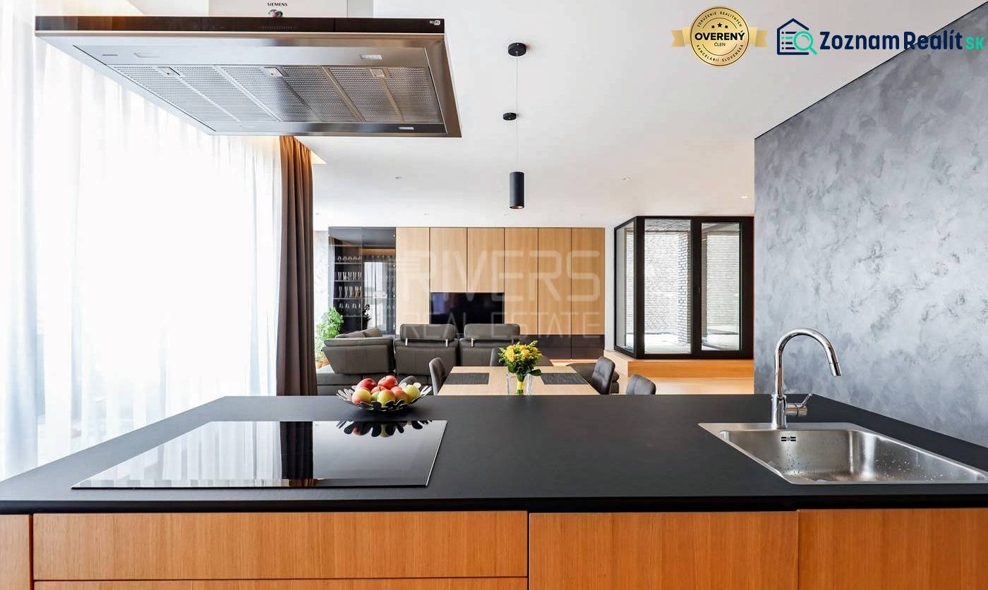 RIVERS I Prémiový 4-izbový byt s panoramatickým výhľadom na mesto - Kuchyňa v 4-izbovom byte so sklenenou stenou a jedálenským stolom s kvetmi.
