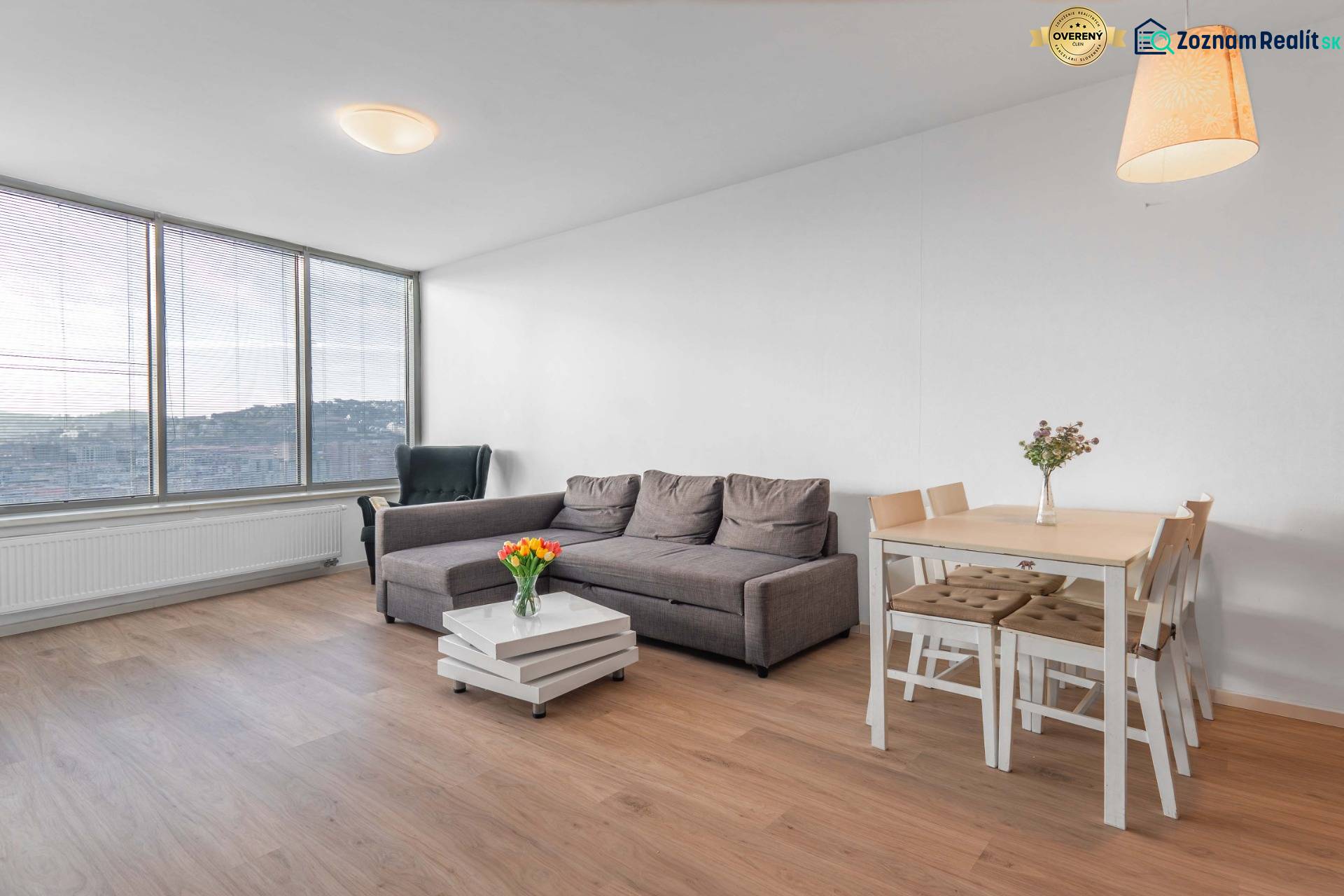 I na predaj 2i byt v komplexe Tri Veže na Bajkalskej - Obývacia izba 2-izbového bytu s podlahou s dreveným dekorom, pohovkou a jedálenským stolom.