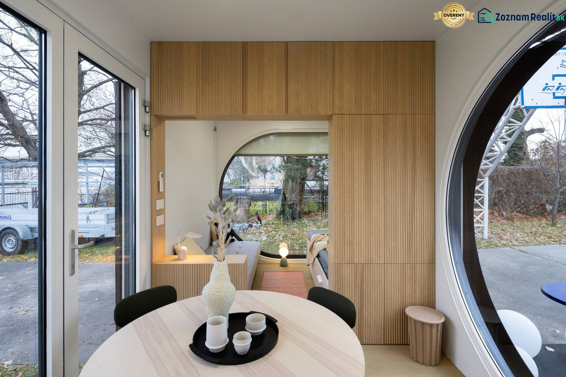 I Predaj Ecocapsule – autonómne ekologické bývanie - Sklenené dvere, drevené dekorácie, okrúhle okno a stôl s nádobami v jedálenskej časti.