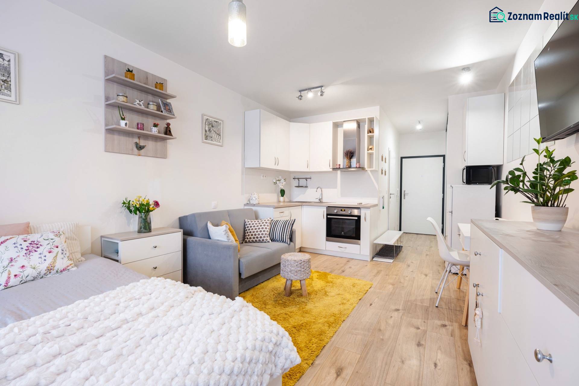 Prenájom 1-izbového bytu, Béžová, Béžová, Petržalka - REZERVOVANÉ - Svetlý interiér 1-izbového bytu s kuchyňou, posteľou a podlahou s dreveným dekorom.