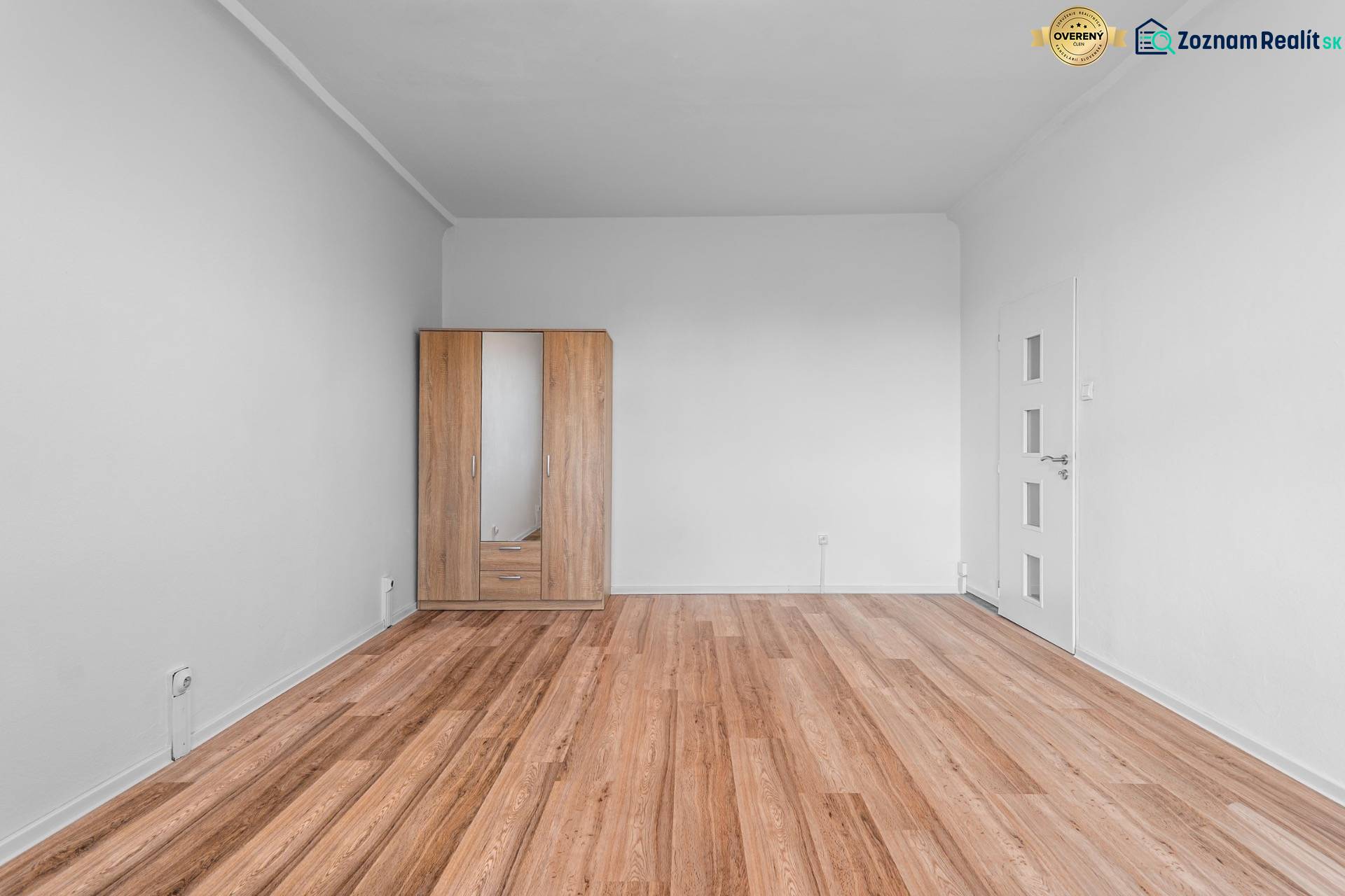 Komfortný 1,5-izbový byt s balkónom v Ružinove na predaj - Izba s bielymi stenami, podlaha s dreveným dekorom, šatník so zrkadlom, 1-izbový byt.