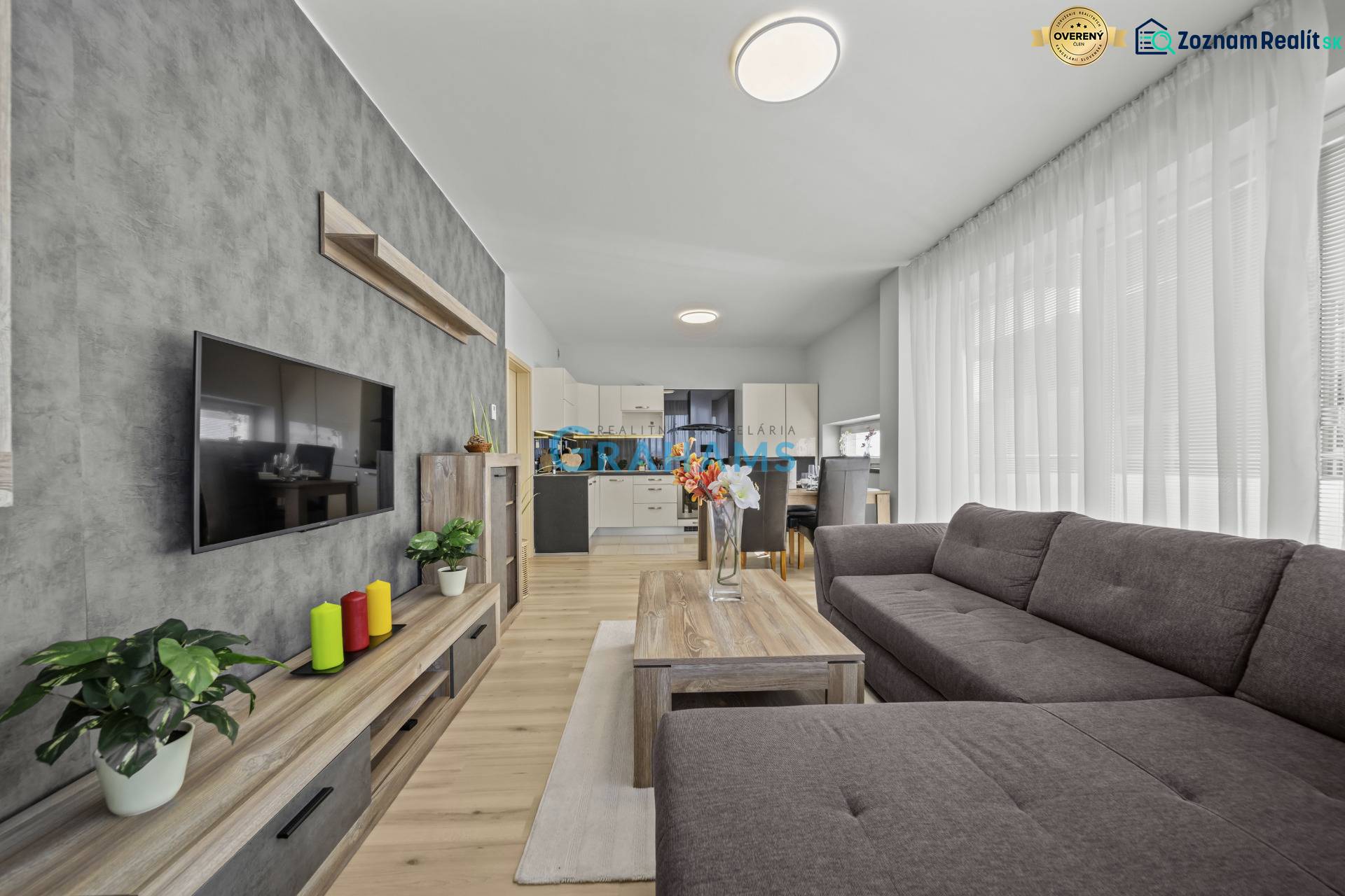 Svetlý 3-izbový byt 90 m² s terasou 18,5 m², 2 garáže, Smaragdová ul. - Obývacia izba v 3-izbovom byte s podlahou s dreveným dekorom a sivou sedačkou.