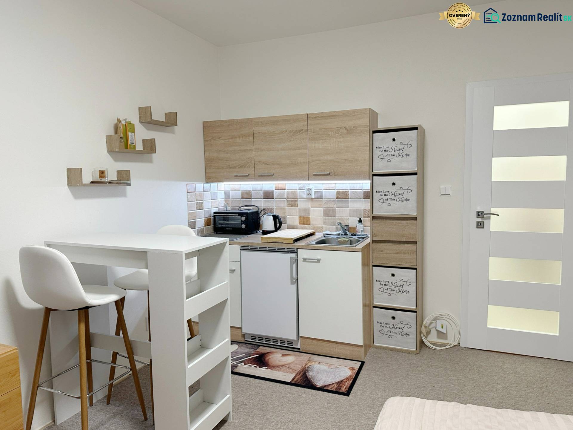 Kompletne zrekonštruovaná garzónka na prenájom, Internátna ulica - Garsónka s kuchynkou, bielym stolom a kreslami, podlaha s dreveným dekorom.